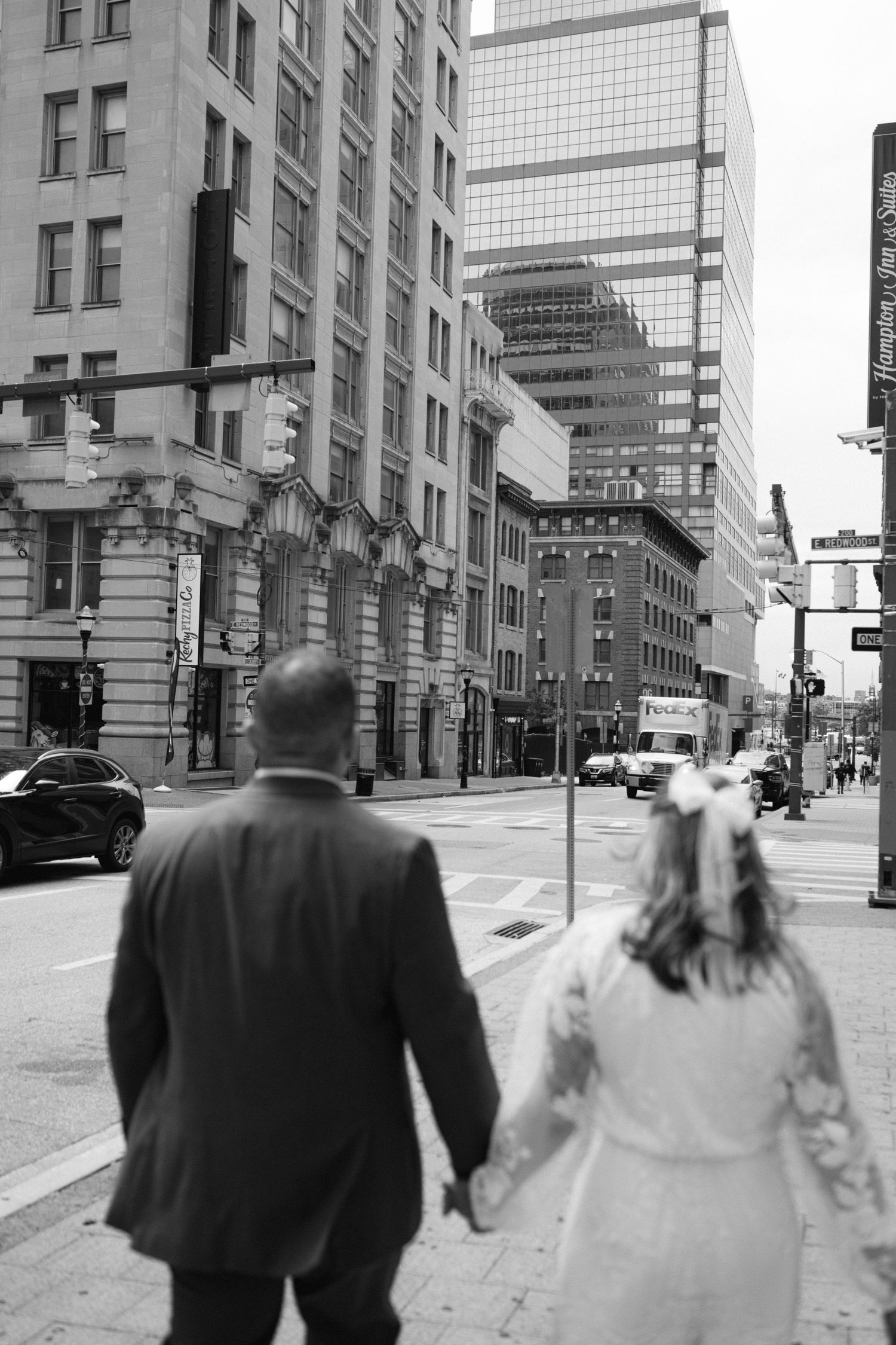A couple walks down a city street with tall buildings and skyscrapers in the background.