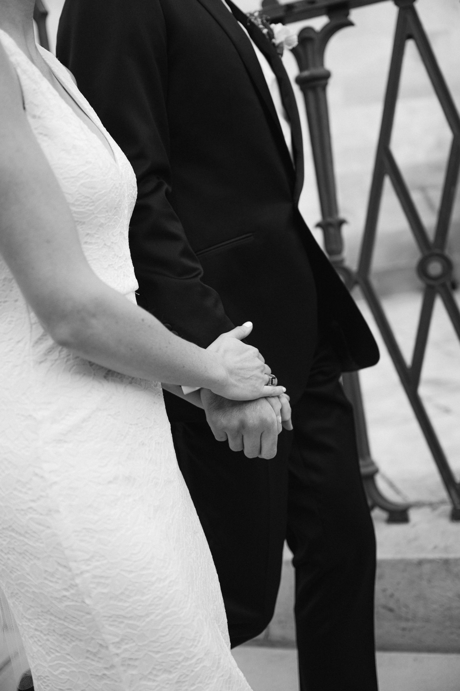Black and white photo of bride in white dress holding hands with groom in formal suit.