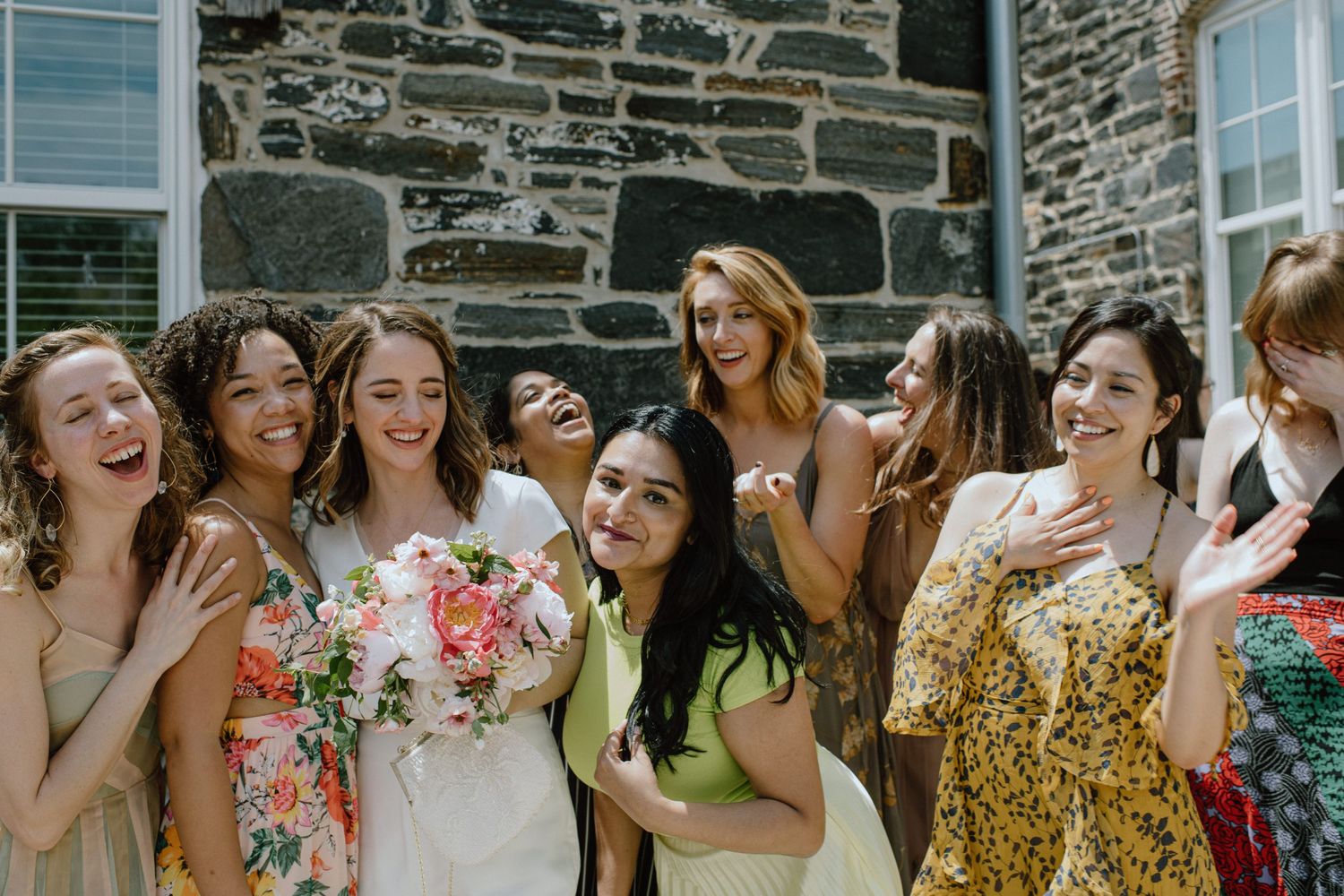Group of women in colorful dresses laughing together at wedding celebration.
