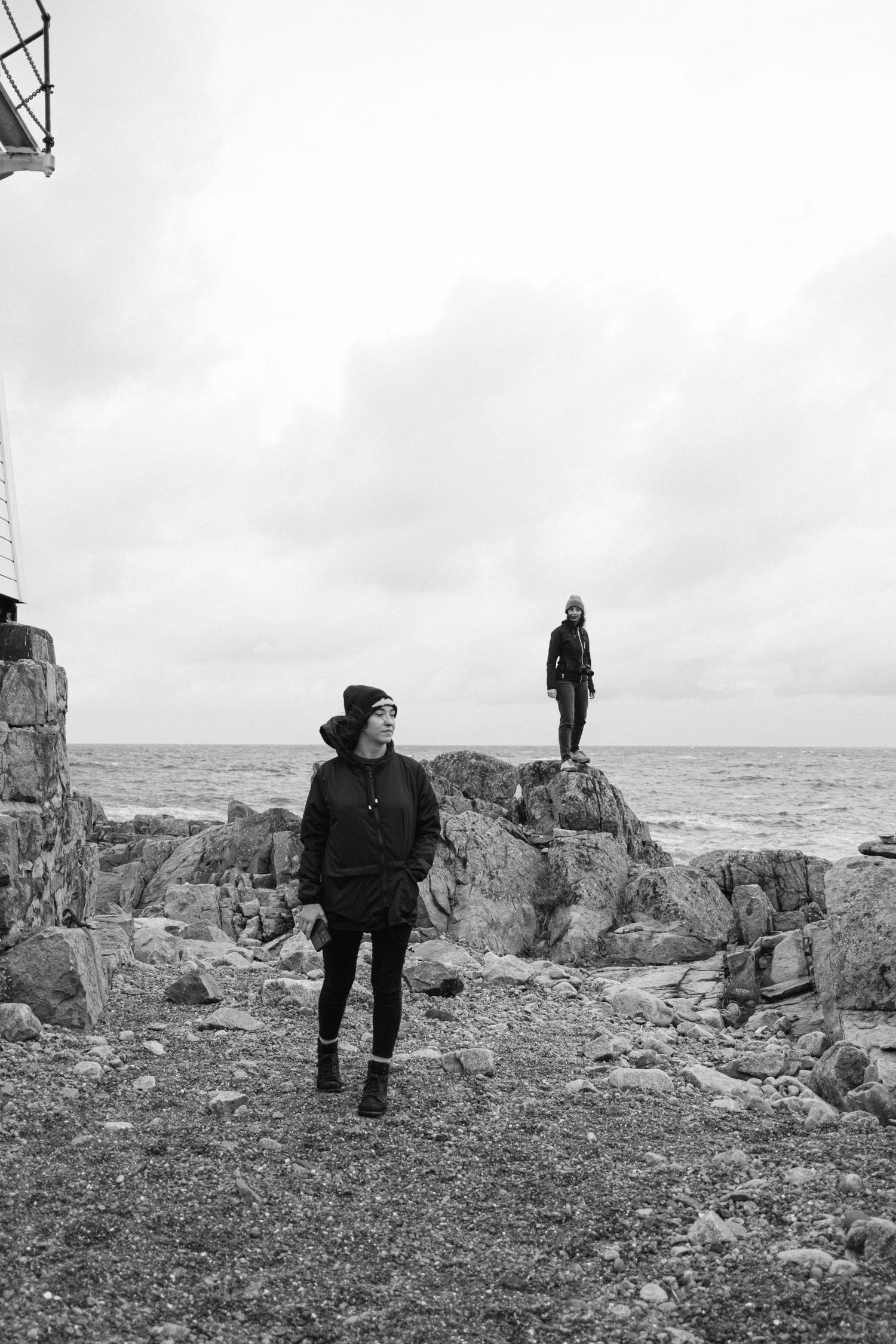 Dramatic black and white coastal landscape with figures on rocky shoreline.