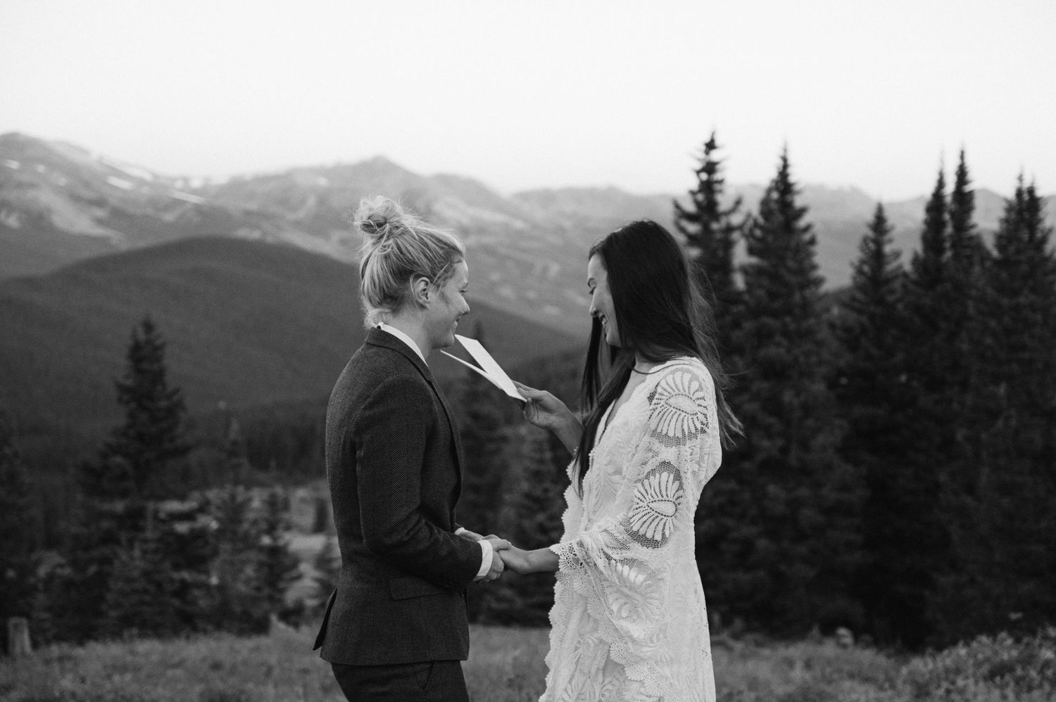A couple sharing an intimate moment against a backdrop of mountain peaks and evergreen trees.