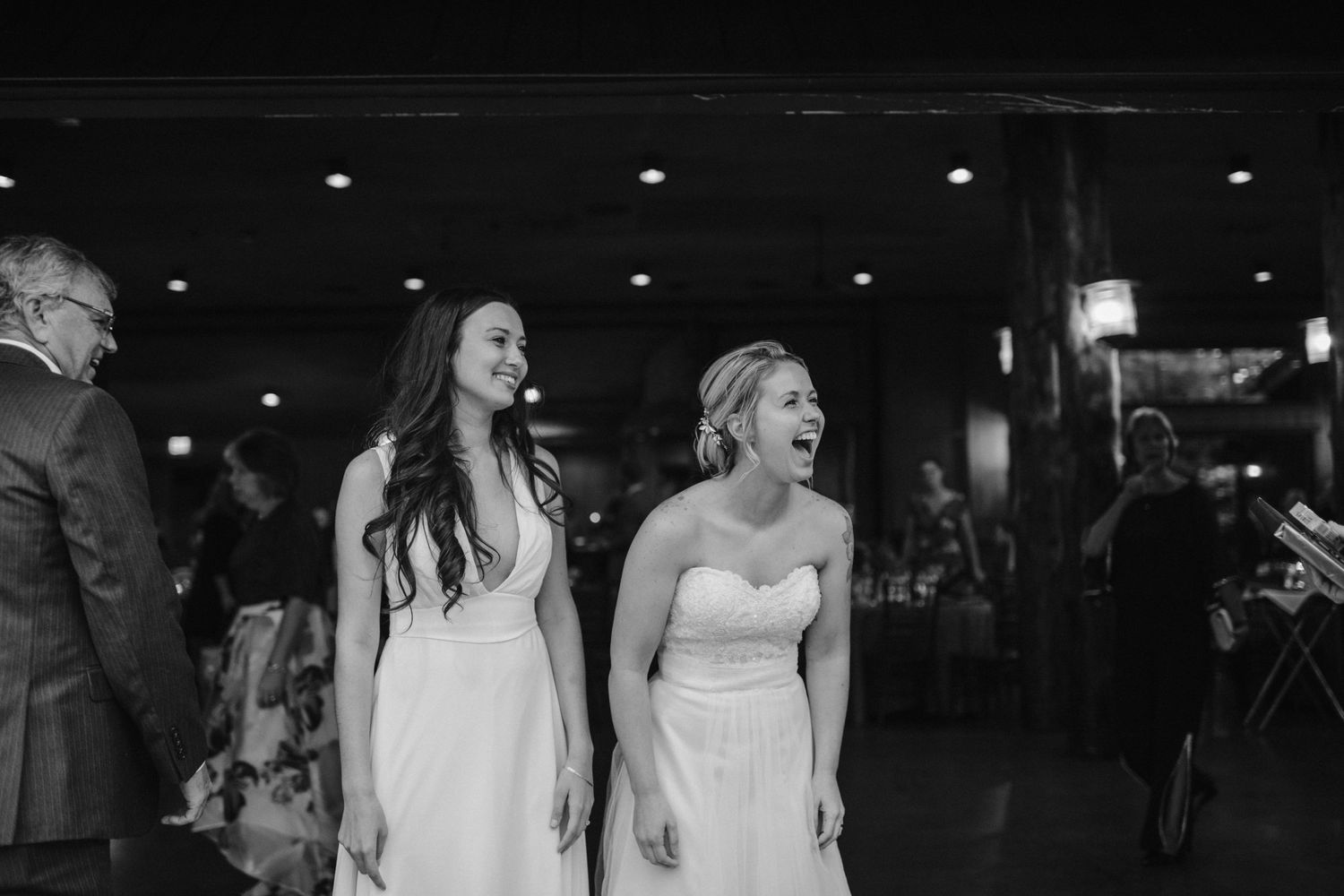 Two people in white dresses share a joyful moment during a wedding celebration.