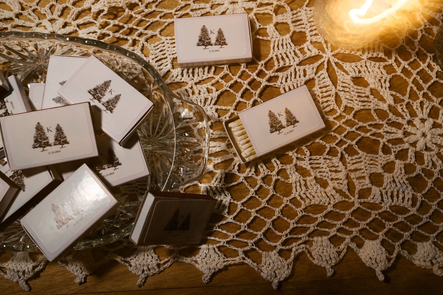 Holiday postcards with tree designs arranged on a vintage lace doily with warm lighting and shadows.