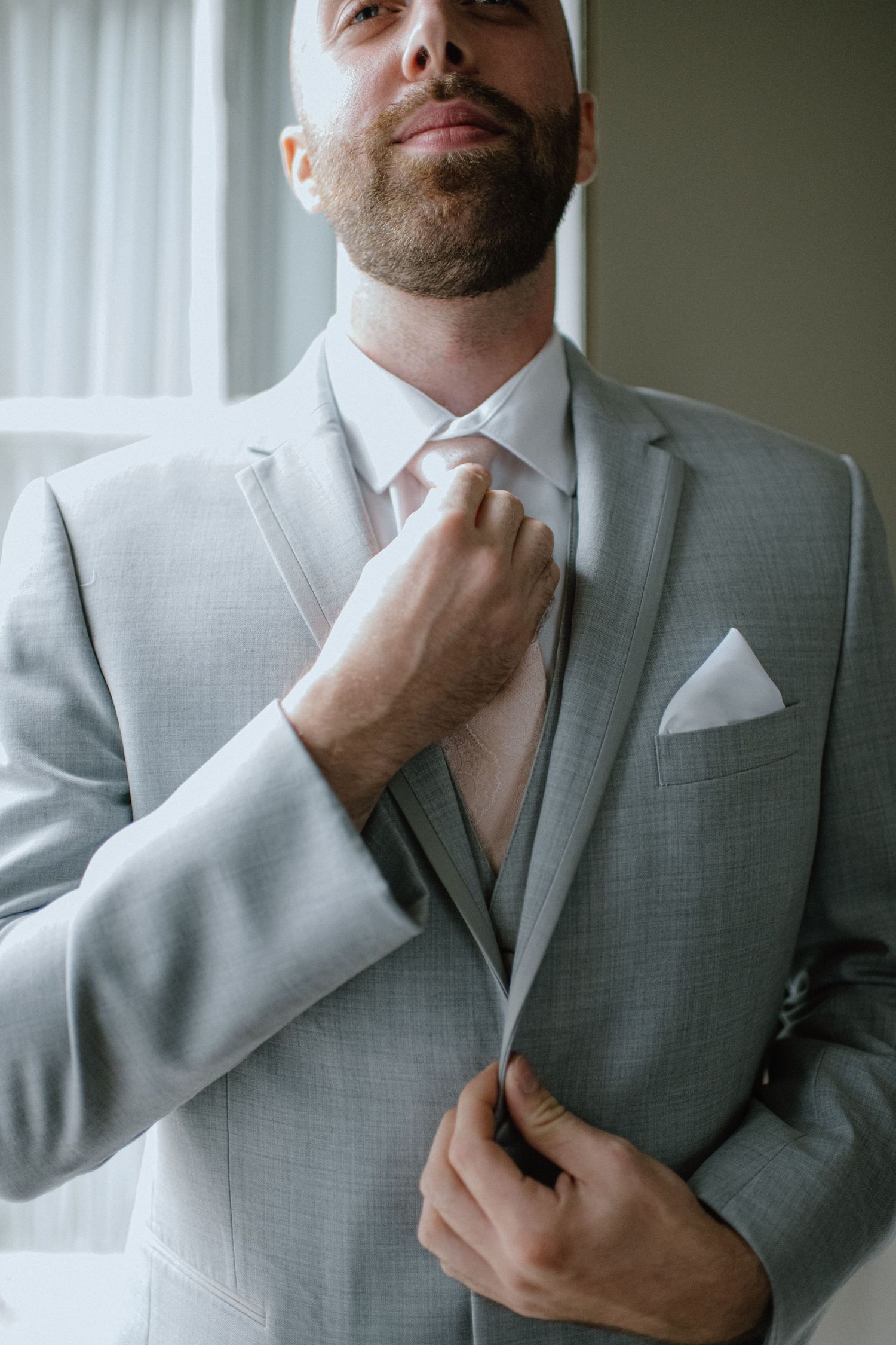 Close-up of groom adjusting his tie while wearing a light gray suit.