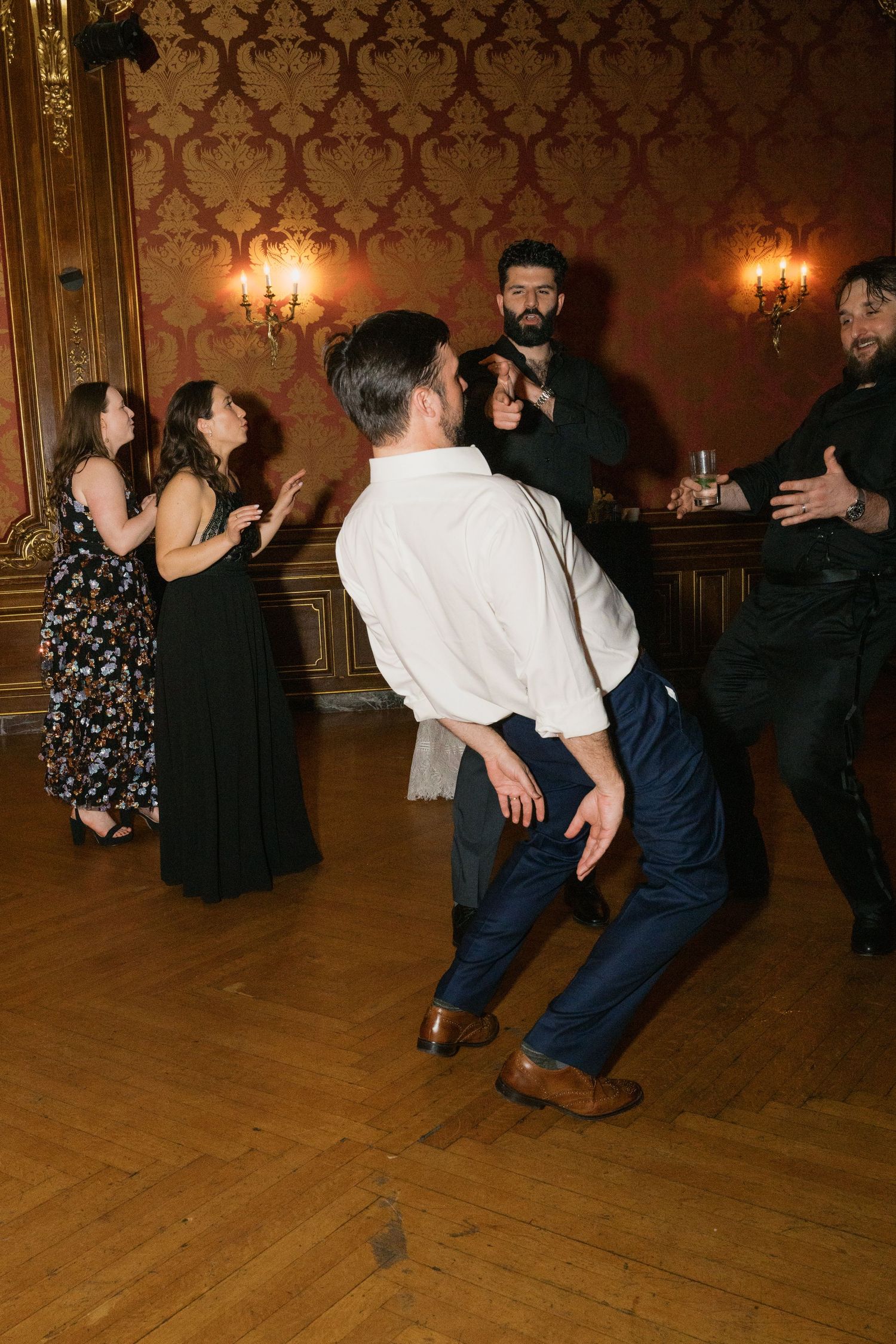 Wedding reception dancers enjoying themselves on wooden dance floor in ornate vintage ballroom.