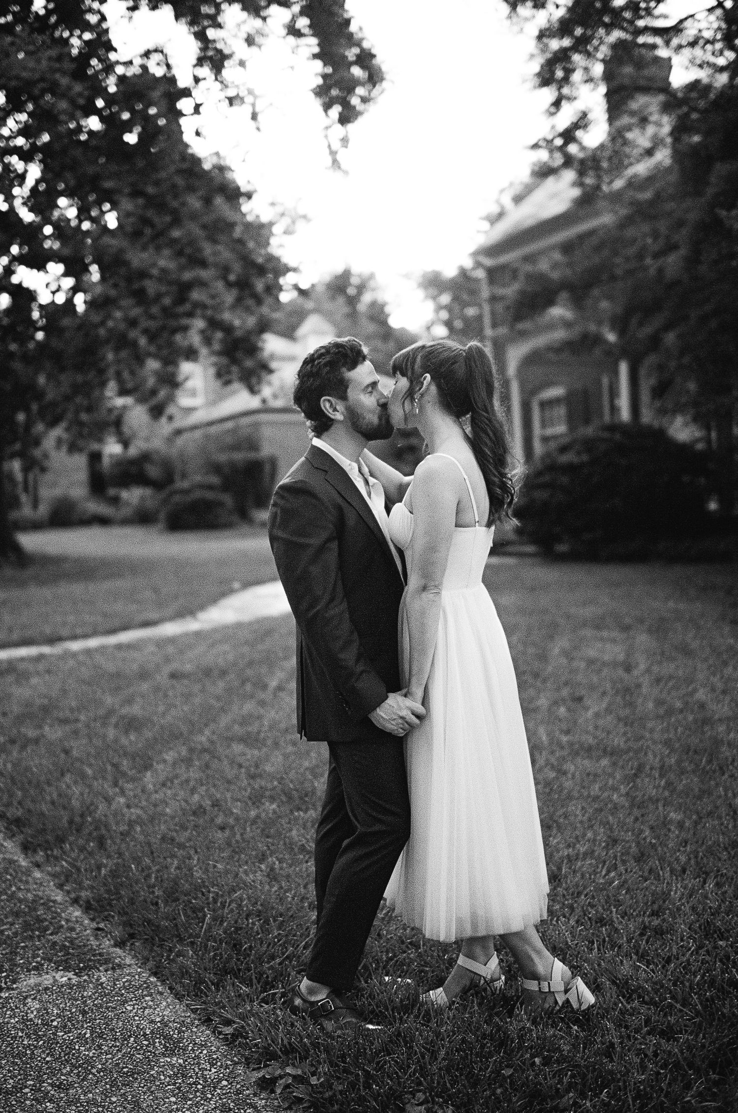 Black and white romantic wedding photo sequence of a couple sharing a tender kiss on grassy lawn.