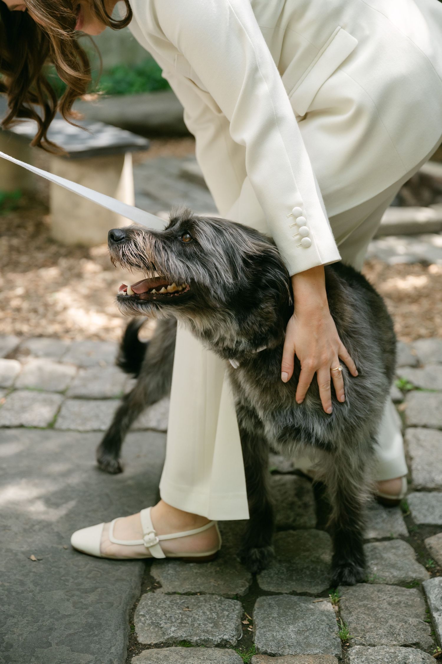 A black shaggy dog receives pets and attention while resting on stone pavement.
