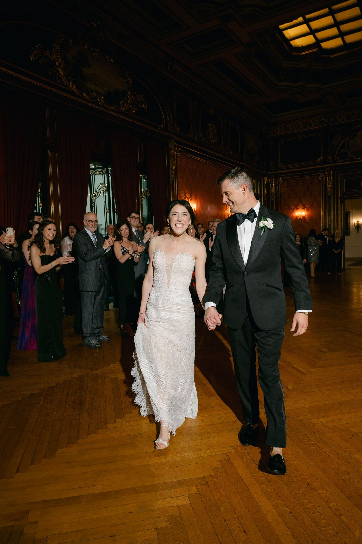 A couple dancing joyfully in a grand ballroom with wooden floors and warm lighting while guests look on at a Baltimore engineers club