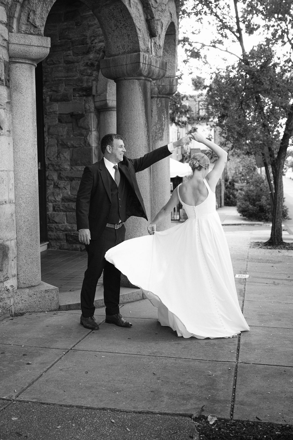 A dancing couple twirls under stone archways during their wedding photoshoot.