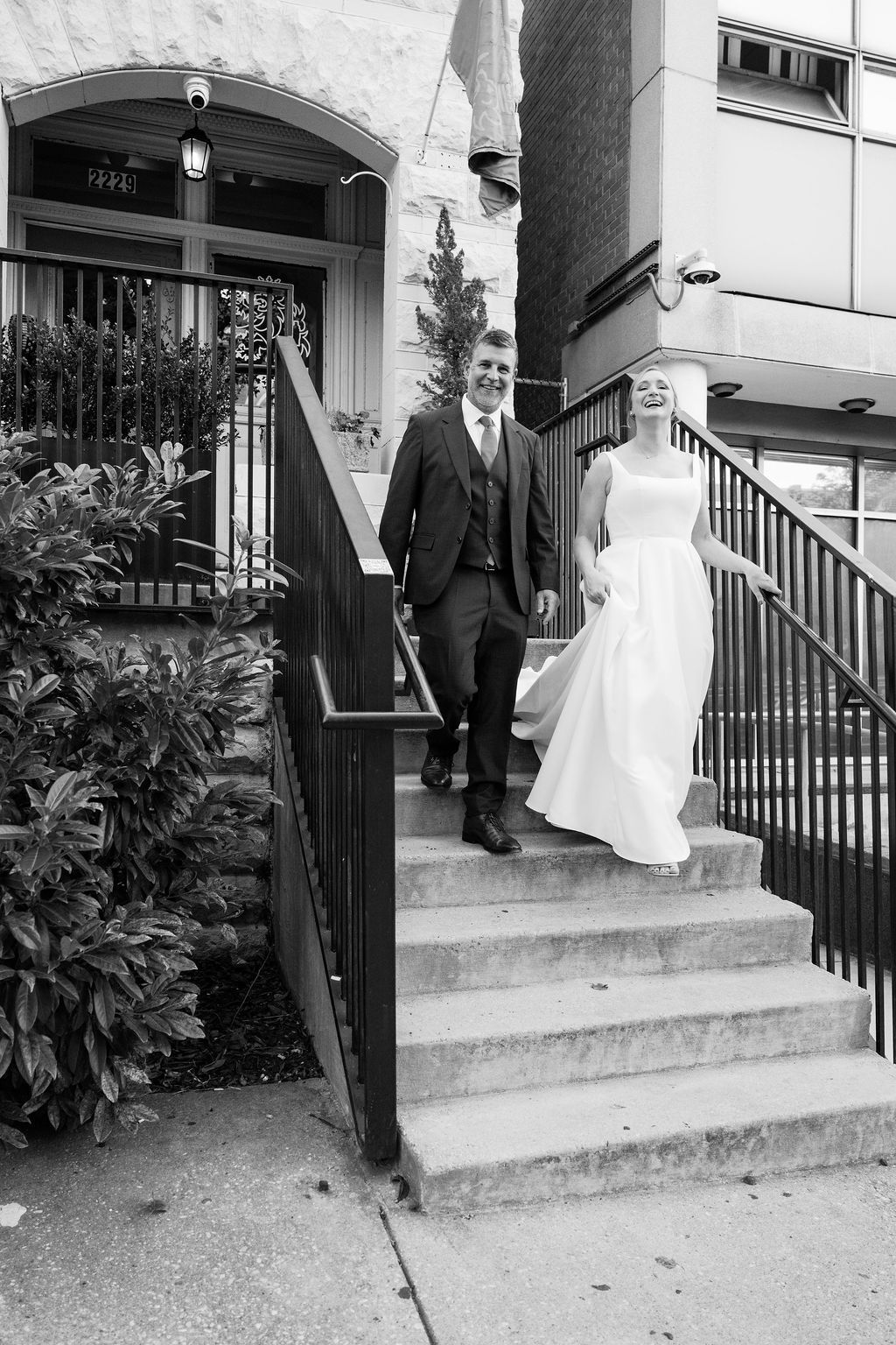 A couple descends stone steps outside a historic building entrance in formal wedding attire.