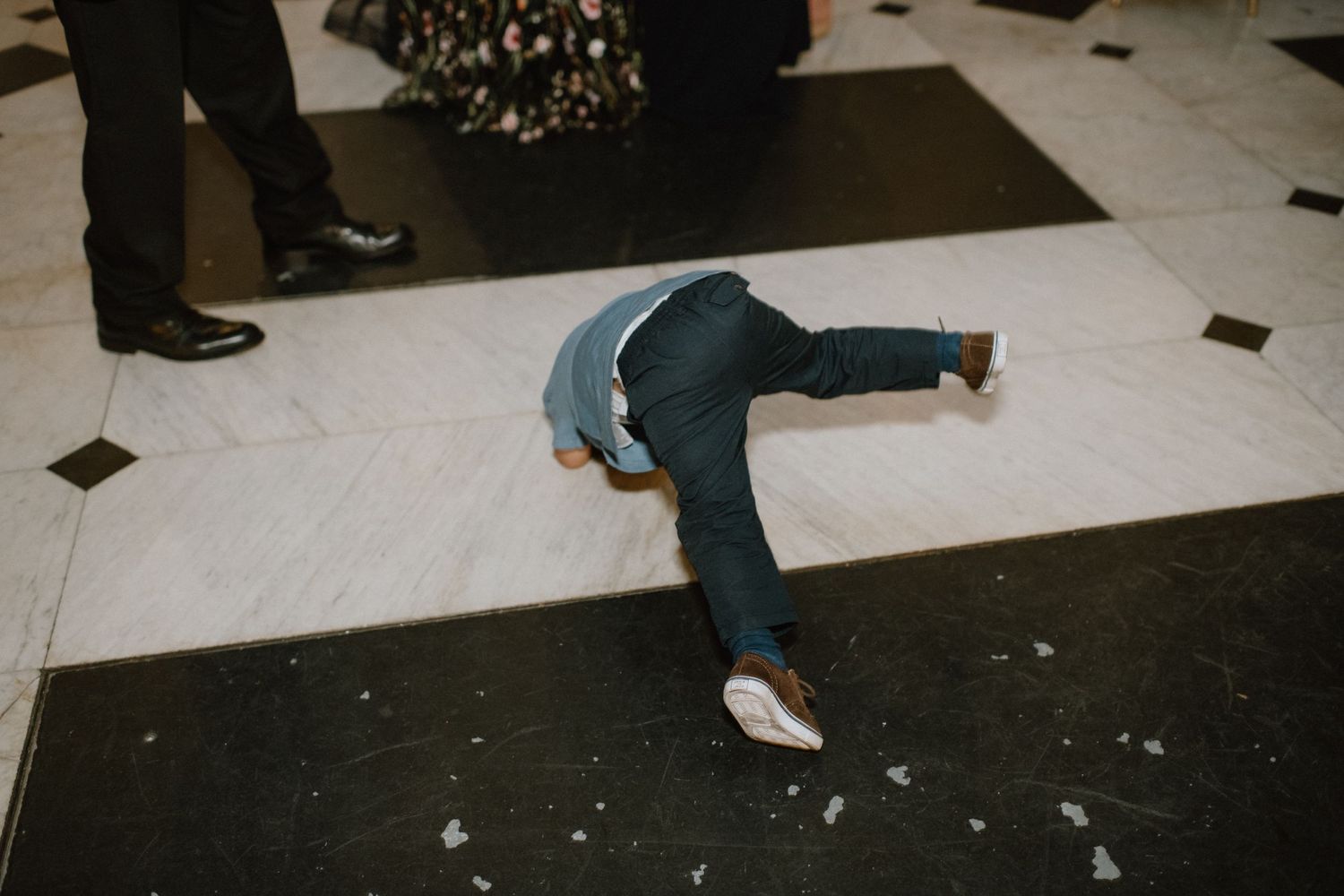 Guest performs dramatic dance move on black and white checkered floor at wedding reception.