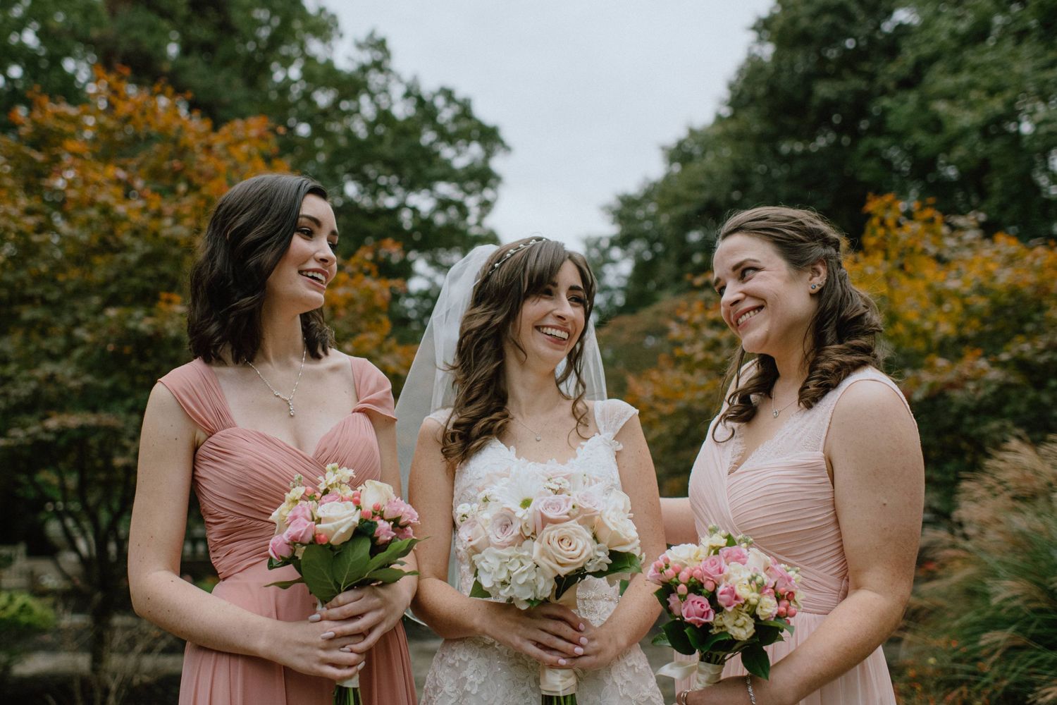 Wedding party in pink dresses holding bouquets while sharing a joyful moment.