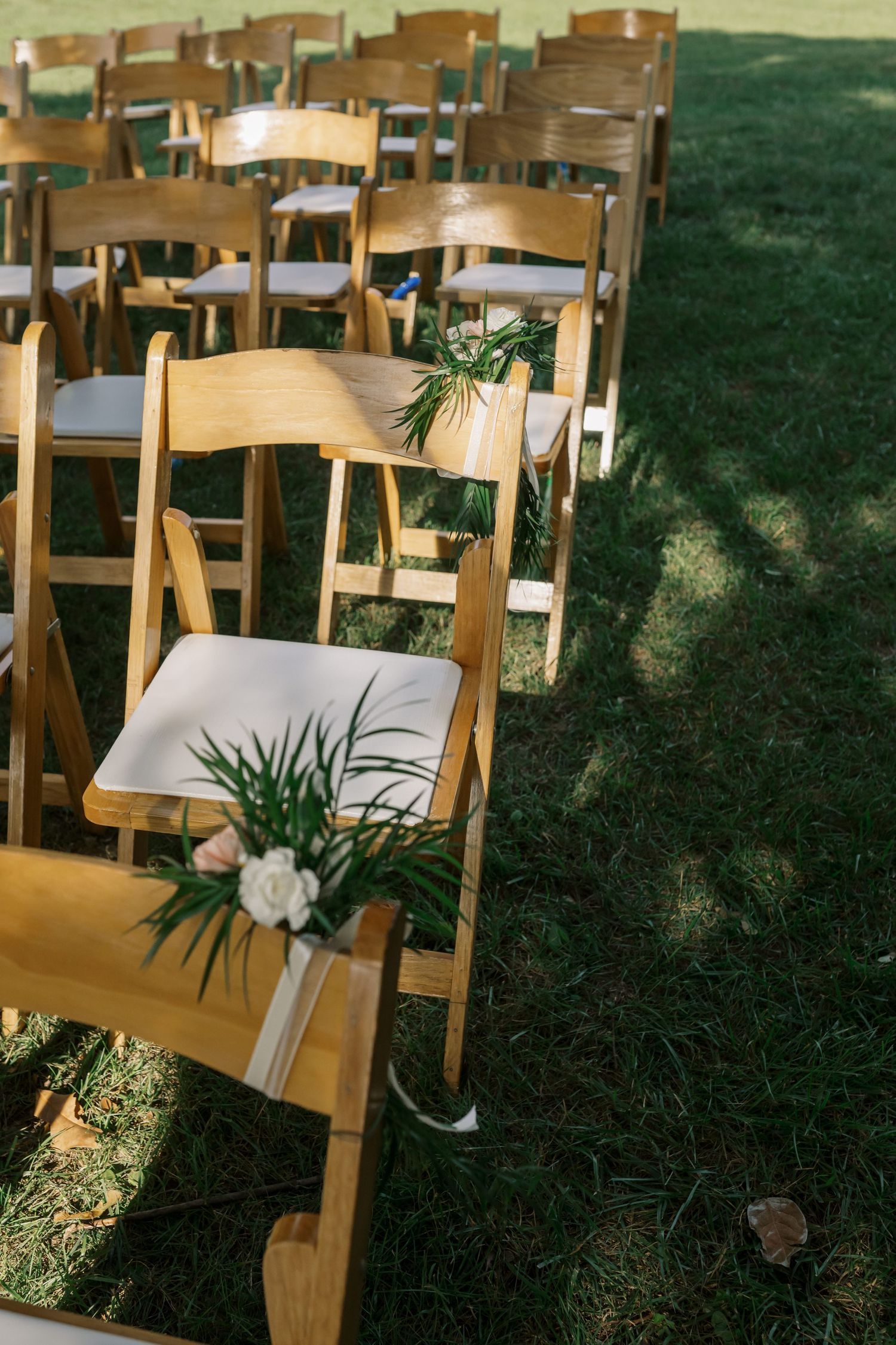 Wooden ceremony chairs decorated with white flowers and greenery arranged outdoors.