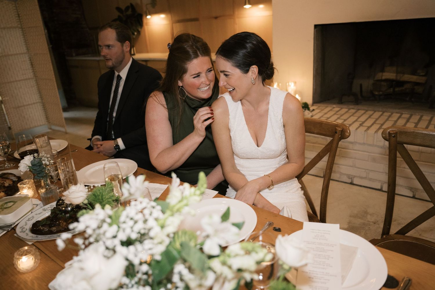 Wedding guests share an intimate moment at a reception table decorated with white flowers and candles.