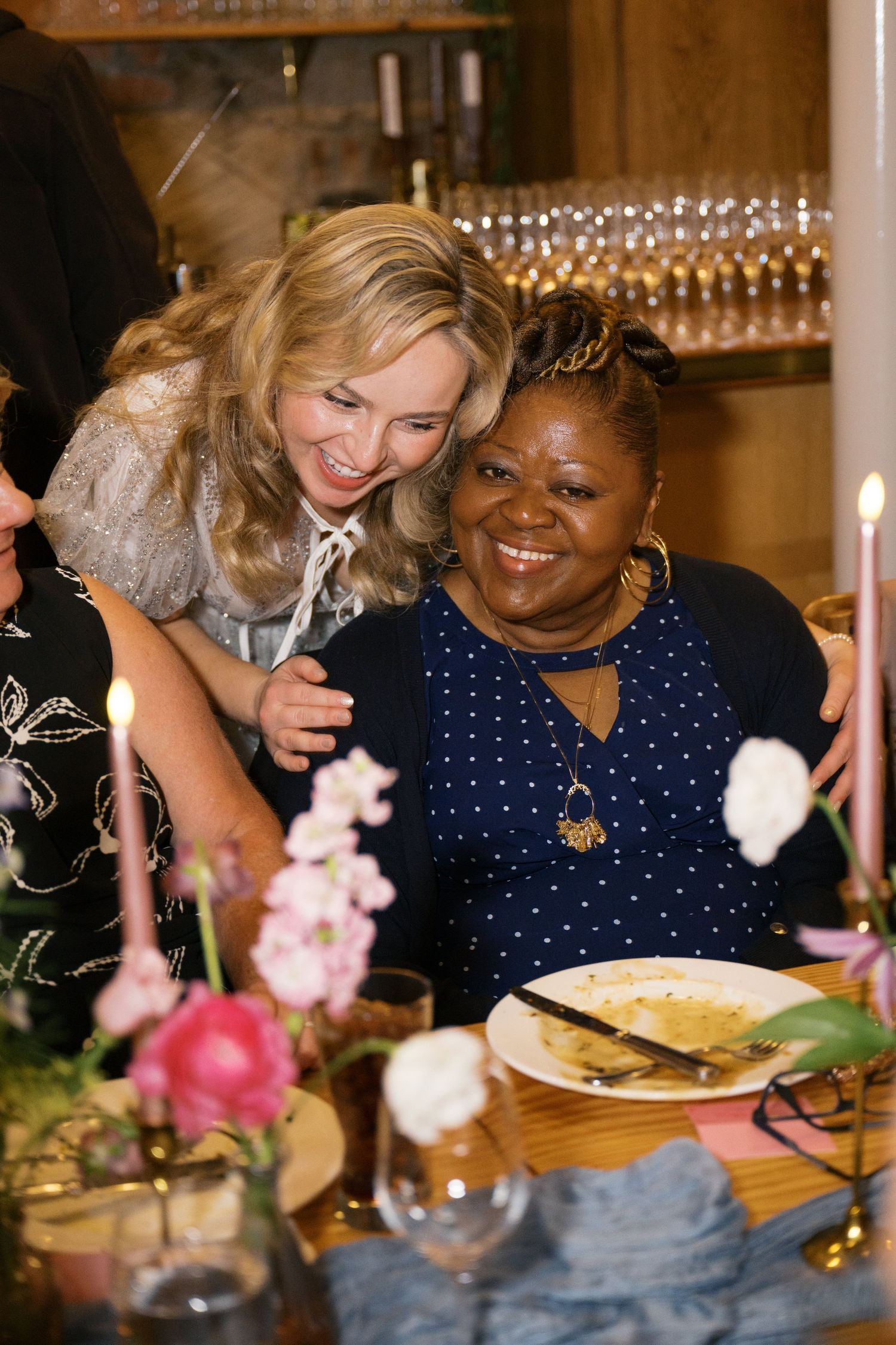 Two guests share a warm moment at a festive dinner table decorated with flowers.