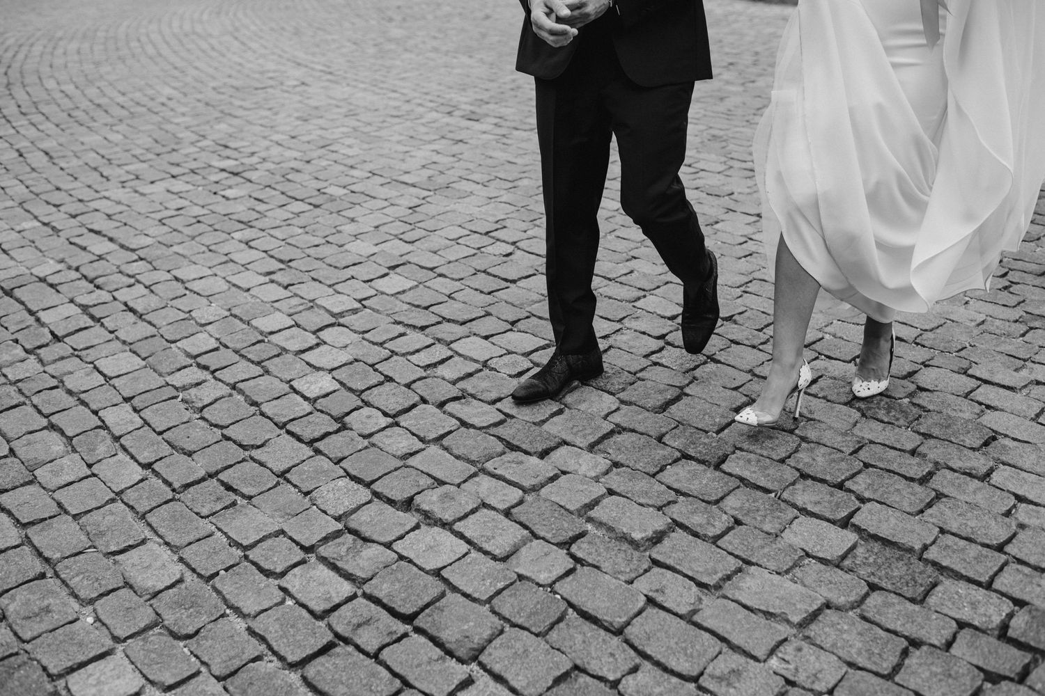 Low angle shot of wedding couple's feet walking on cobblestone street.