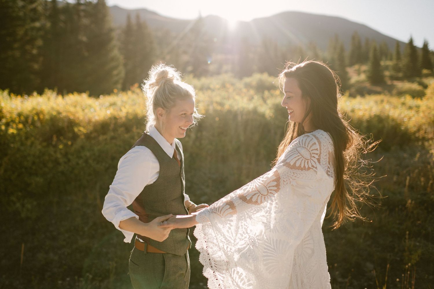 A couple dancing in a mountain meadow at golden hour wearing wedding attire.