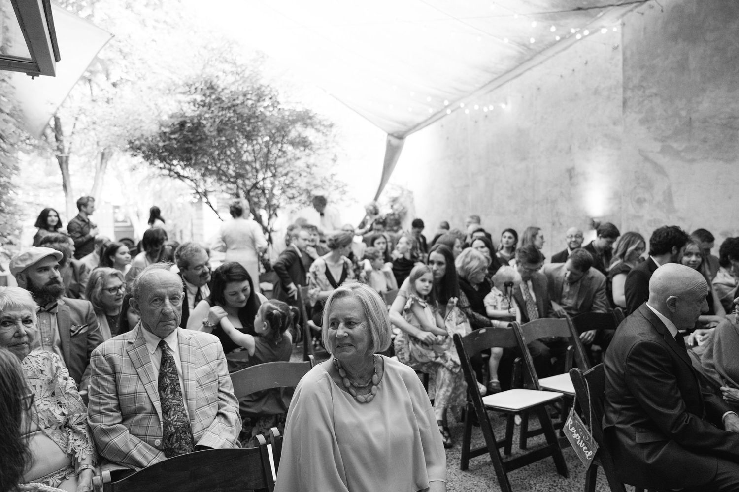 Black and white photo of wedding guests seated outdoors during ceremony.