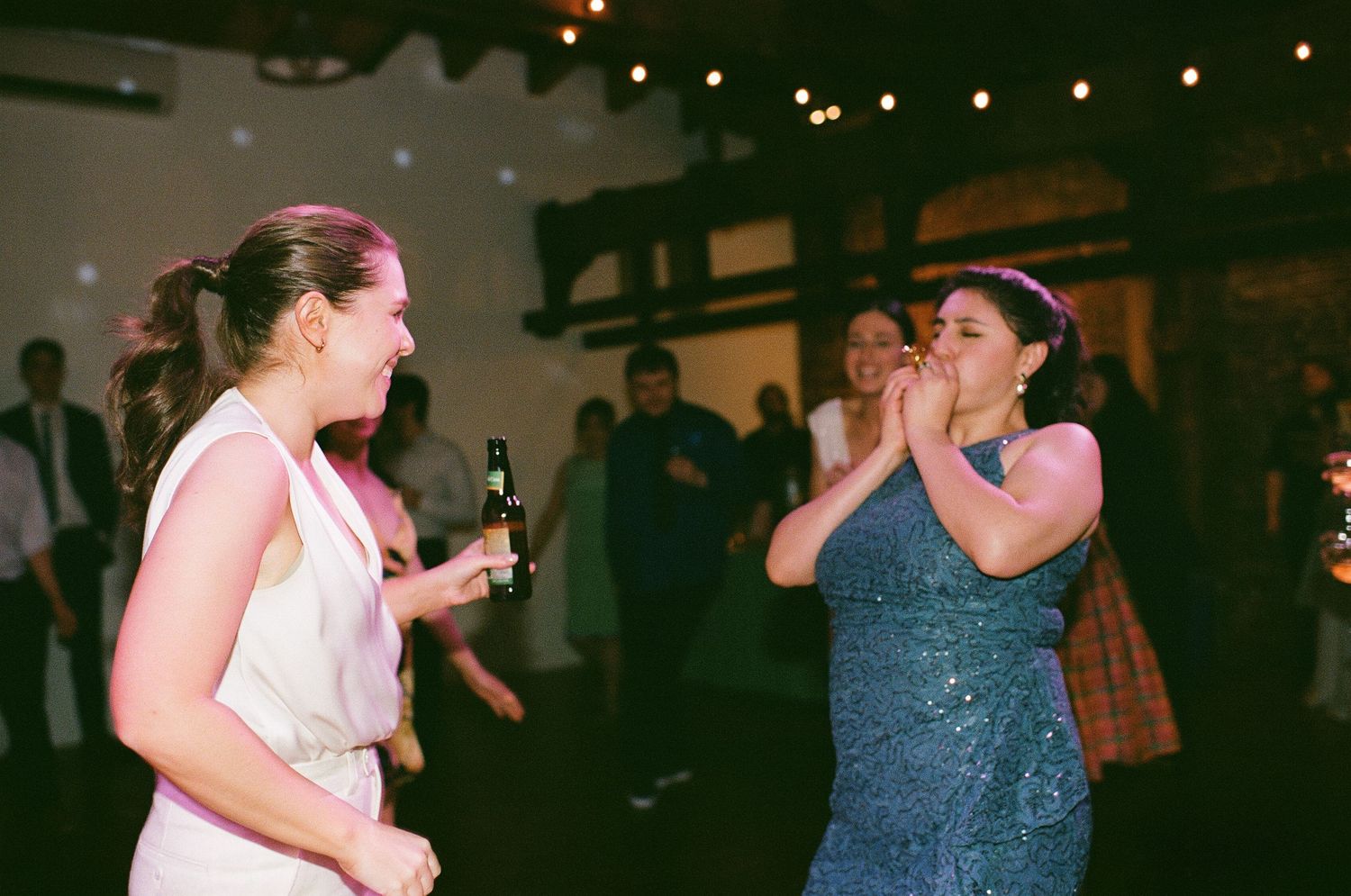 Wedding guests dancing enthusiastically on a dimly lit dance floor with string lights overhead.