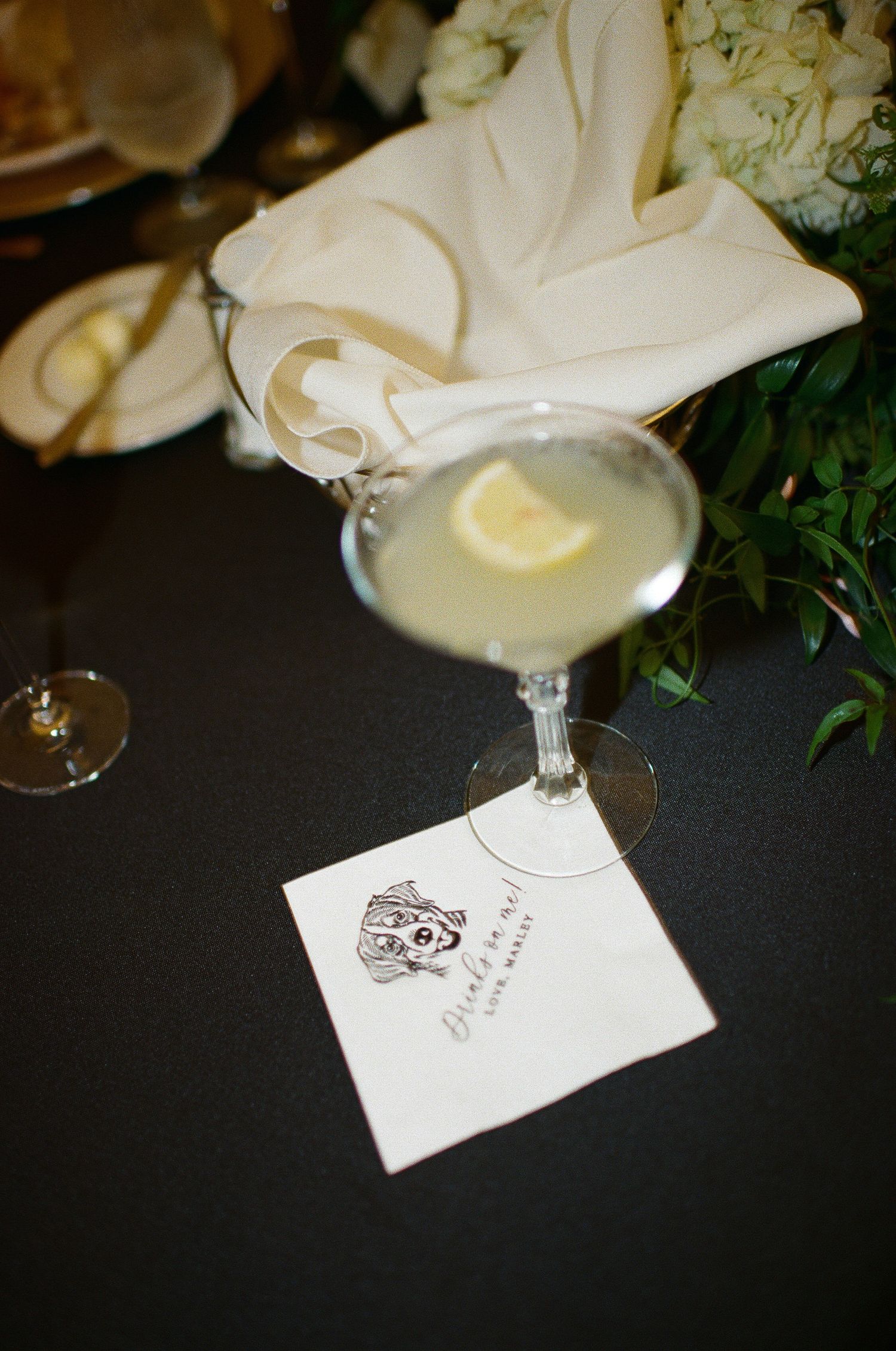 White cocktail napkins and floral arrangements on dark table settings at wedding reception.