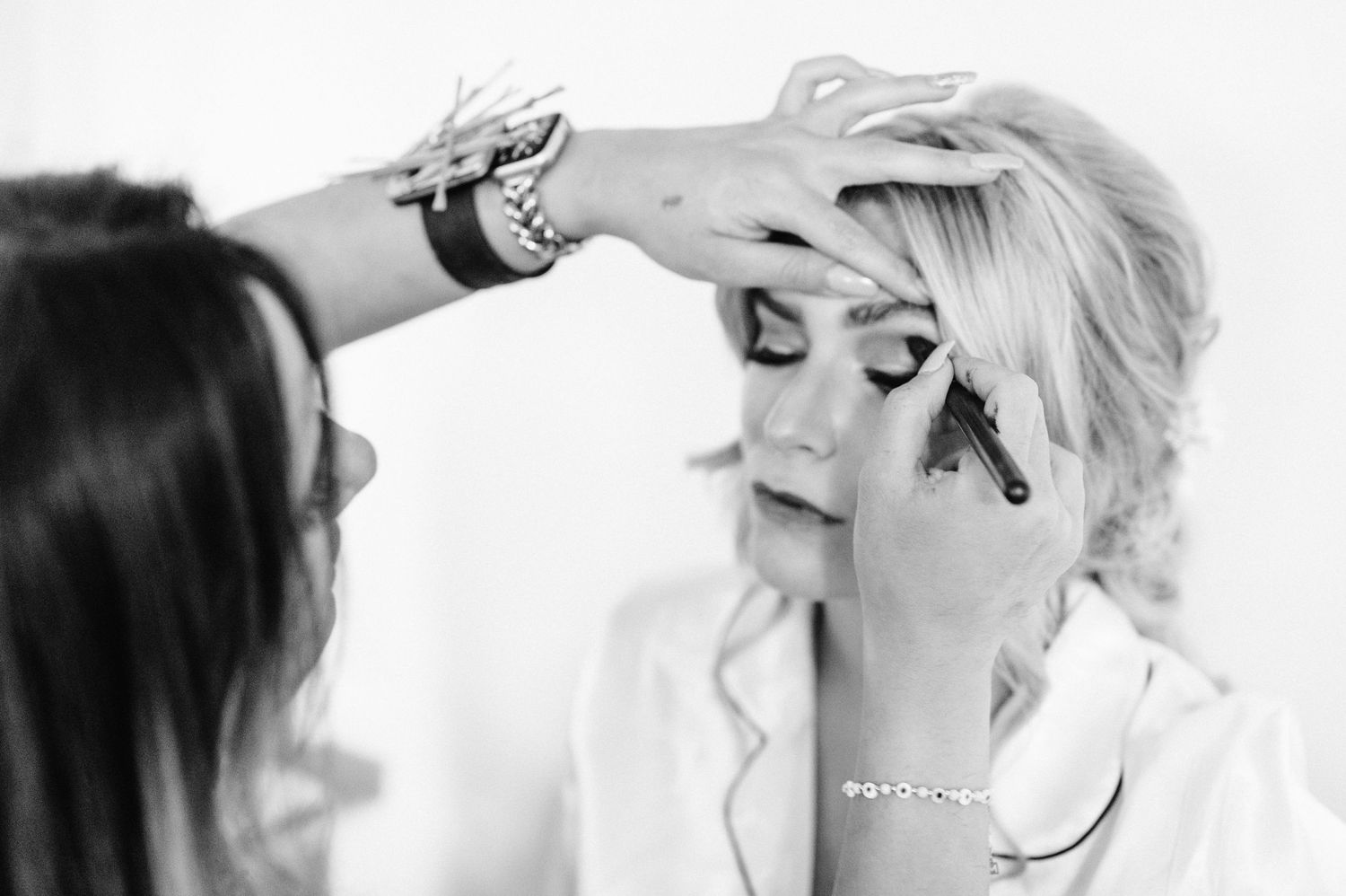 A black and white photo showing the finishing touches of bridal makeup preparation.