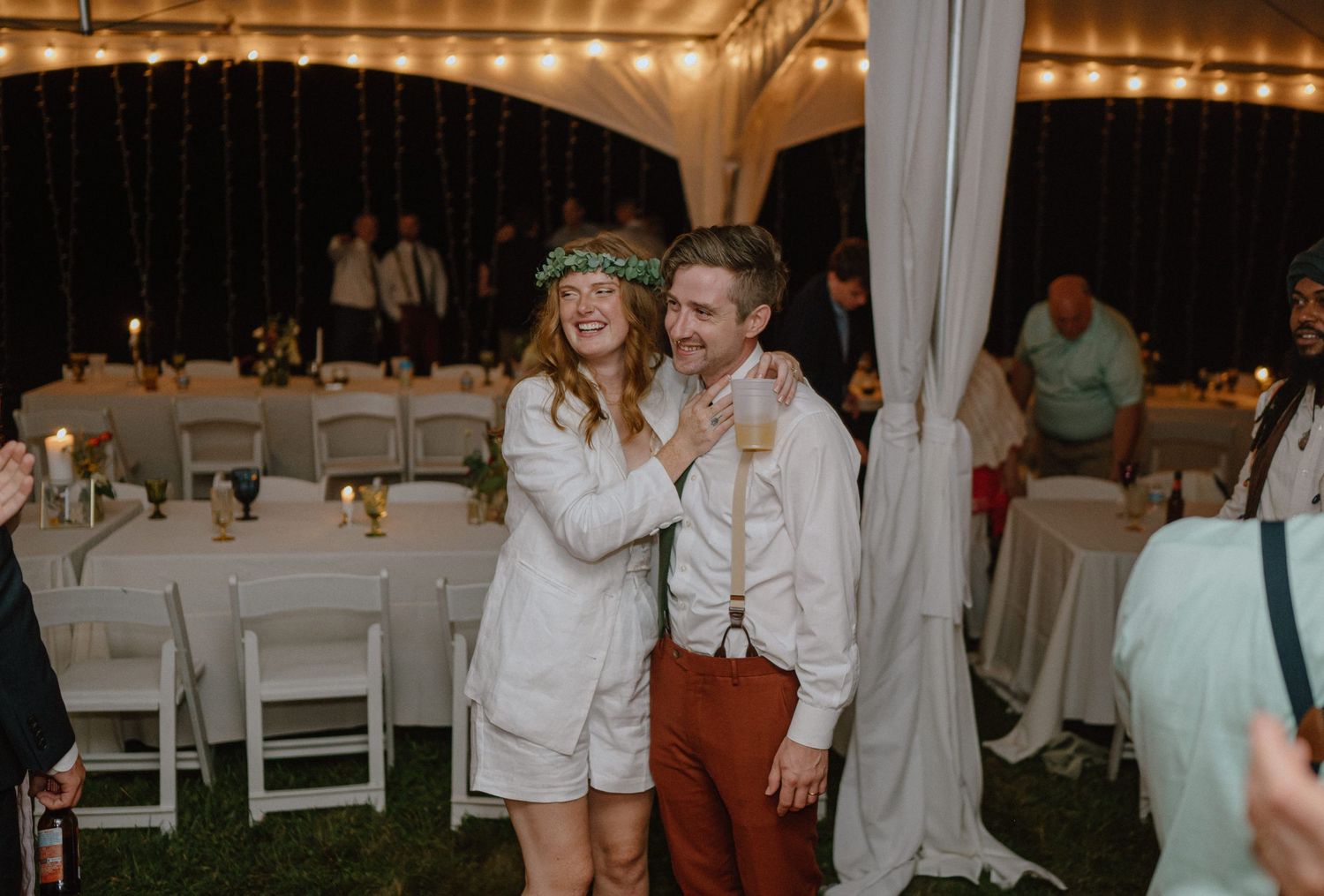 Couple in matching white outfits dancing at their outdoor wedding reception.
