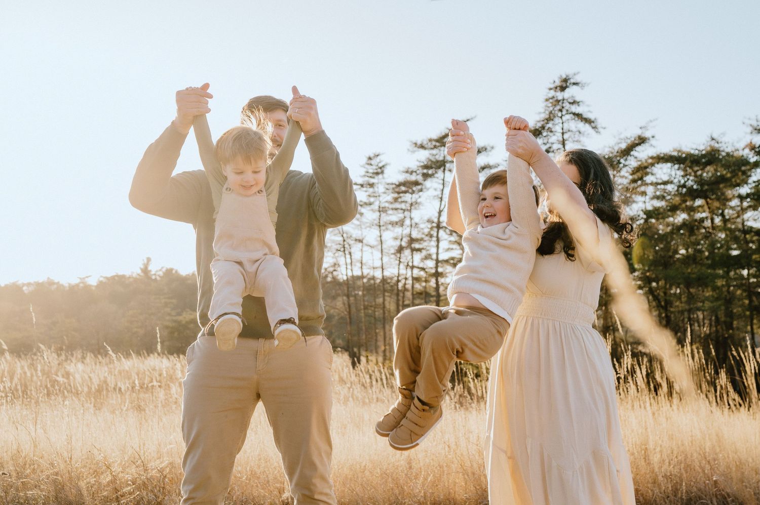 Family playing and lifting children in sunlit field during golden hour.
