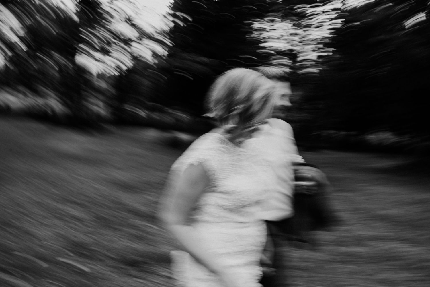 Motion-blurred black and white photo of someone in a white dress outdoors.