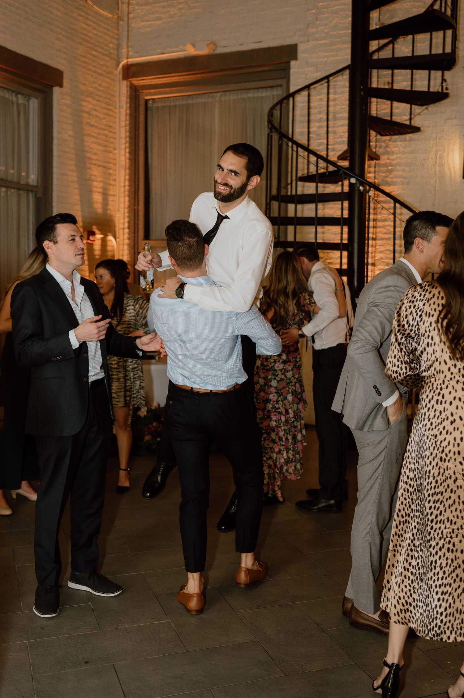 Guests socializing and having fun at an indoor wedding reception with a spiral staircase.