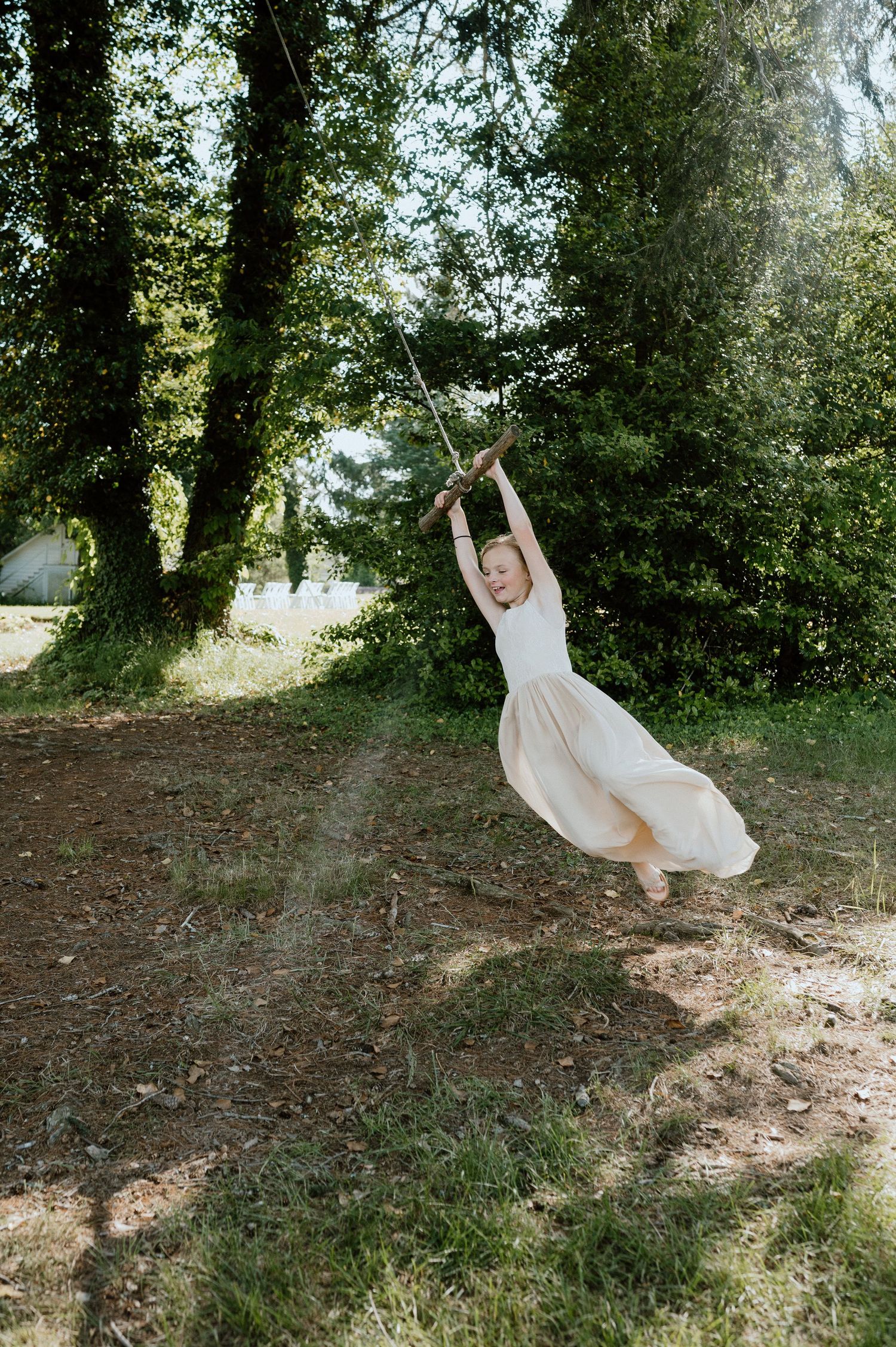 A person in a white dress swings joyfully on a rope swing in a sunlit garden setting.