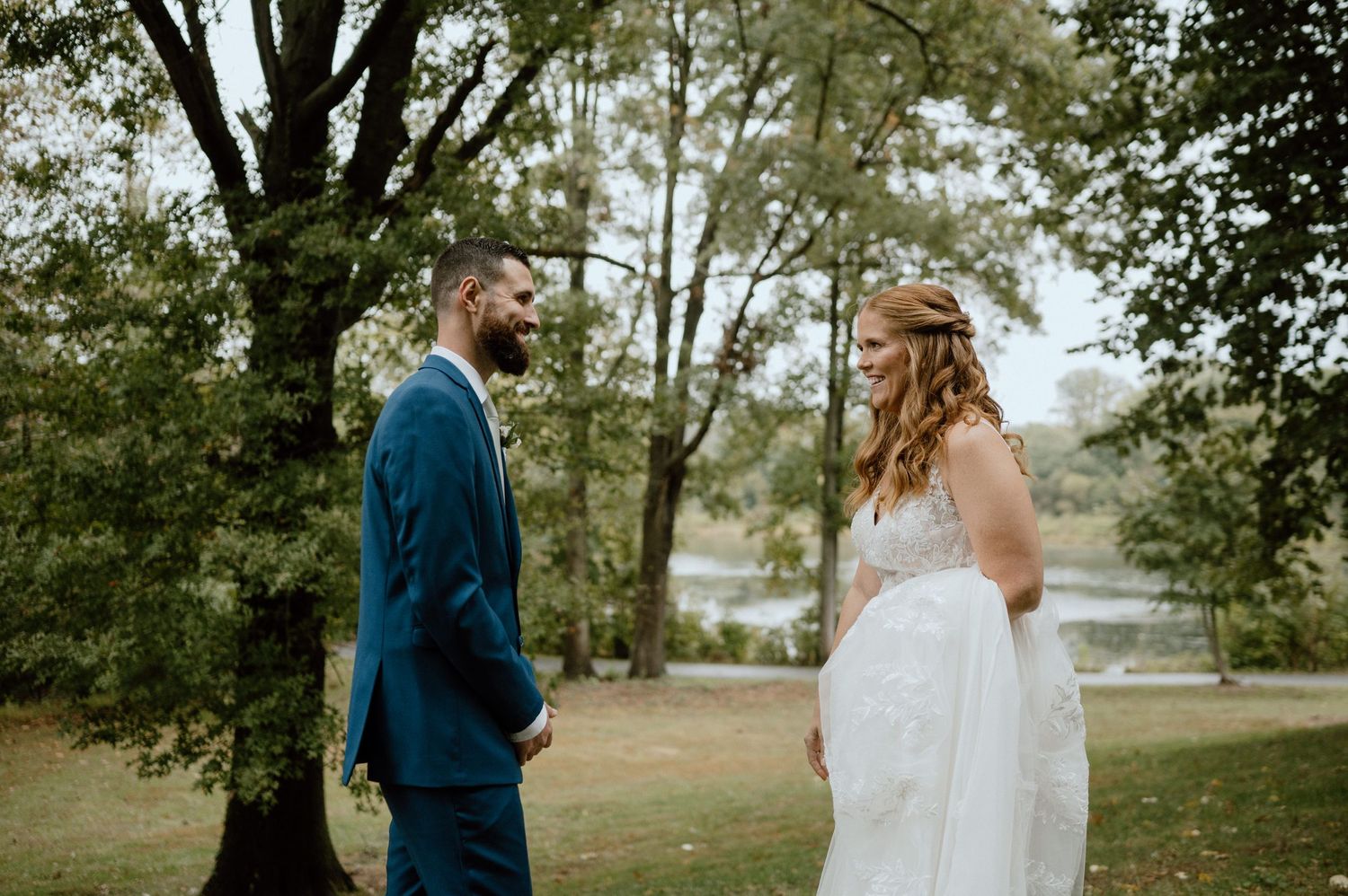 Couple in wedding attire standing together outdoors surrounded by green trees and nature.