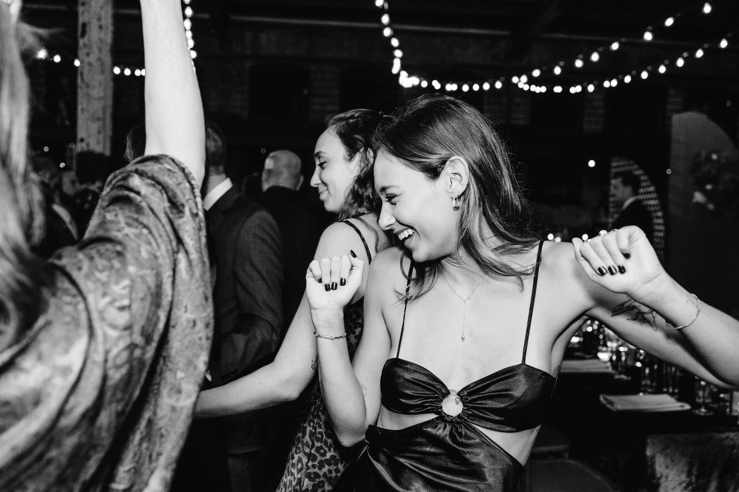 Energetic party scene with people dancing under string lights in a dark venue.