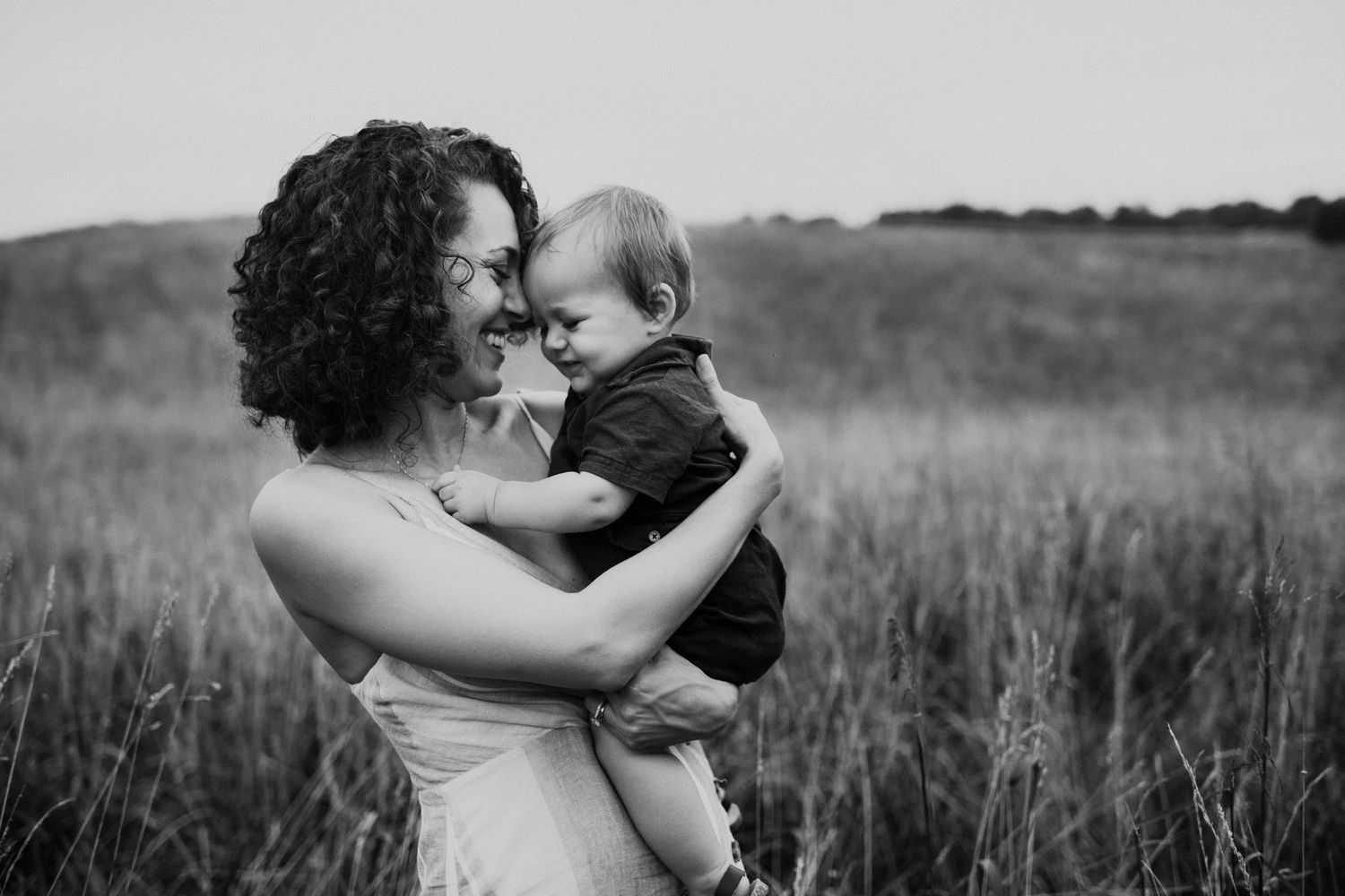 Outdoor family photo in grassy field with baby perched on shoulders during sunset.