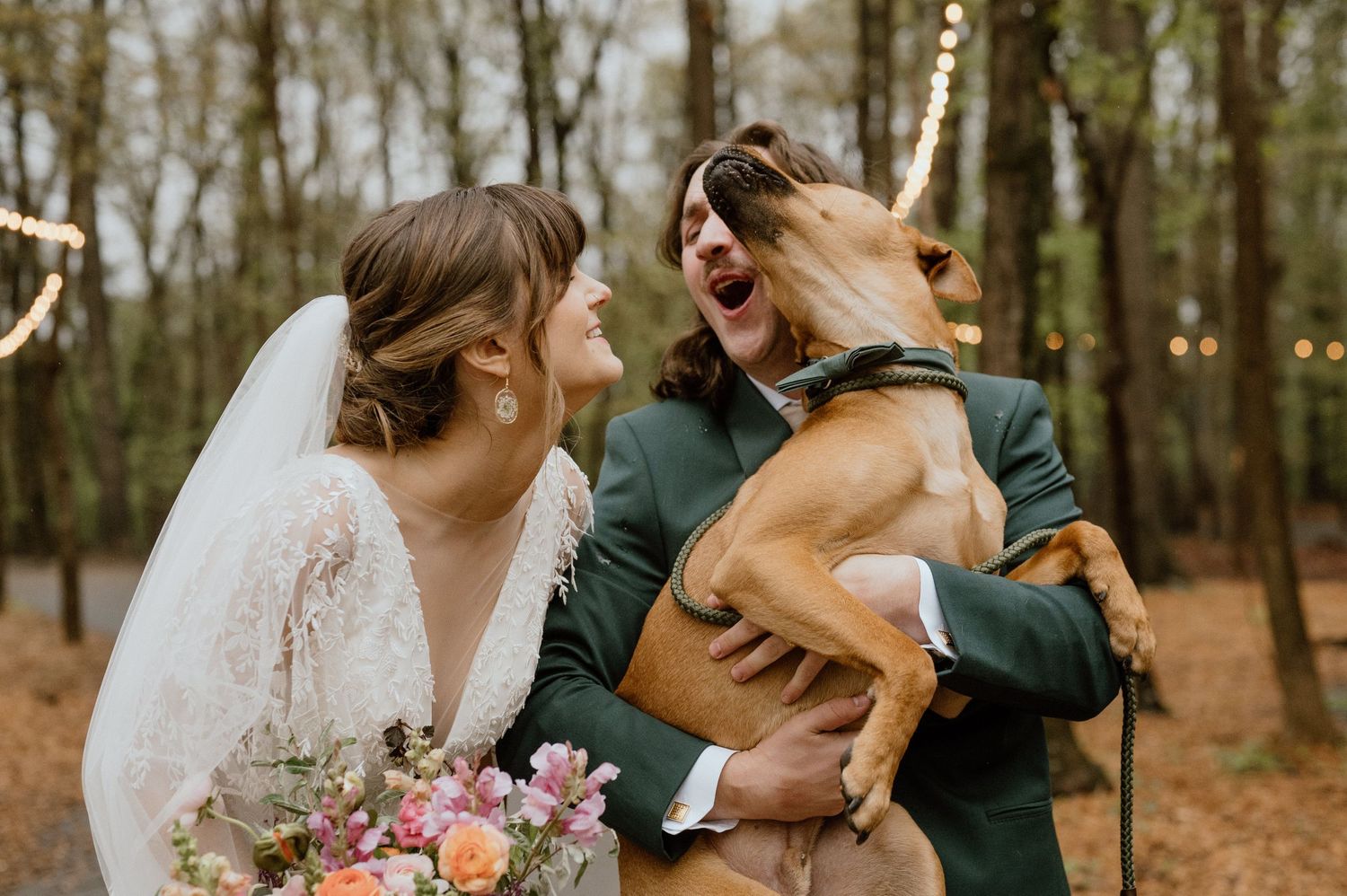 A couple shares a joyful moment with their dog during their wedding photoshoot in the woods.