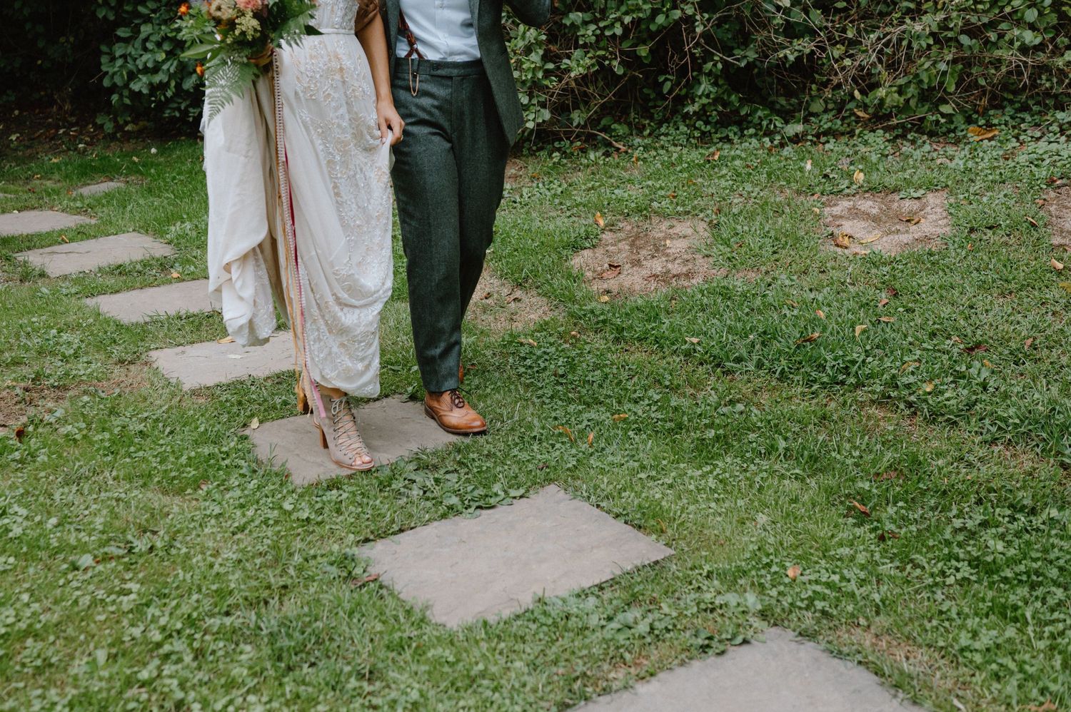 Wedding couple's feet walking on stone garden path surrounded by grass.