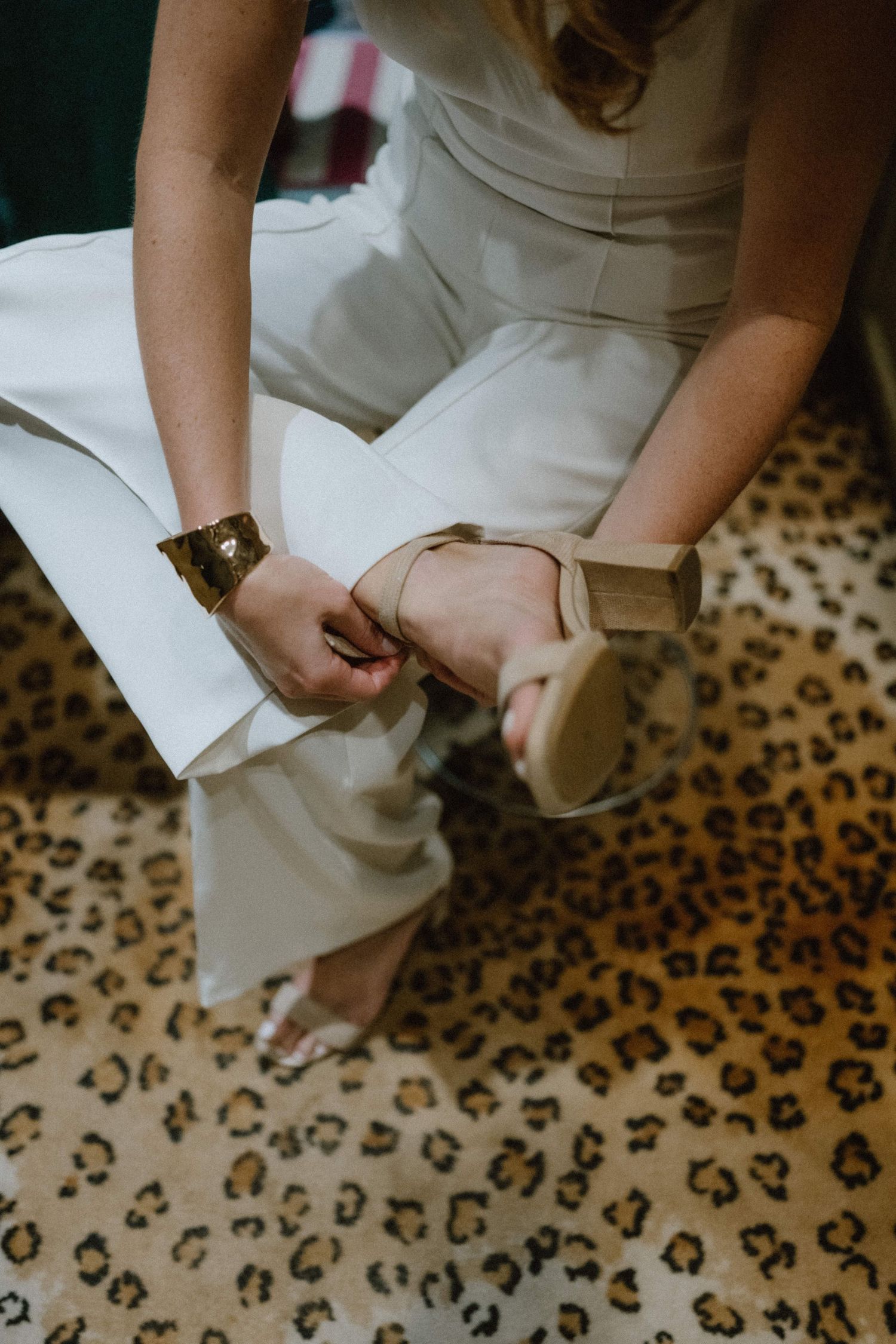 Close-up of someone adjusting footwear while sitting on a leopard print carpet.