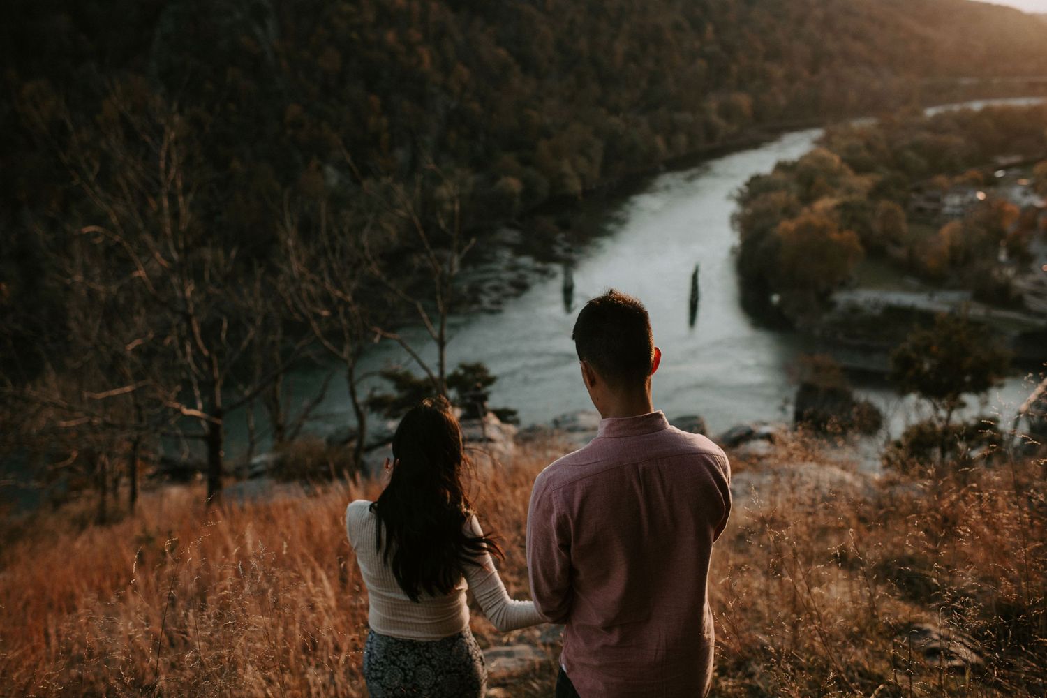 Couple standing on hilltop overlooking winding river during golden hour.