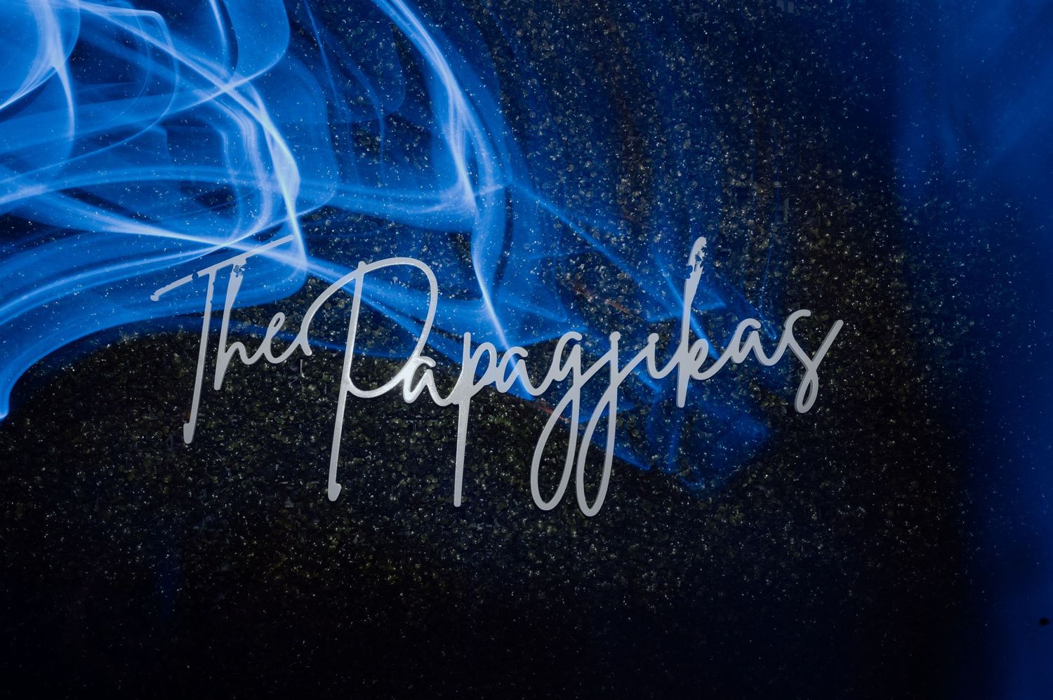 Blue neon cursive signature text glowing against a dark background with smoky effects.