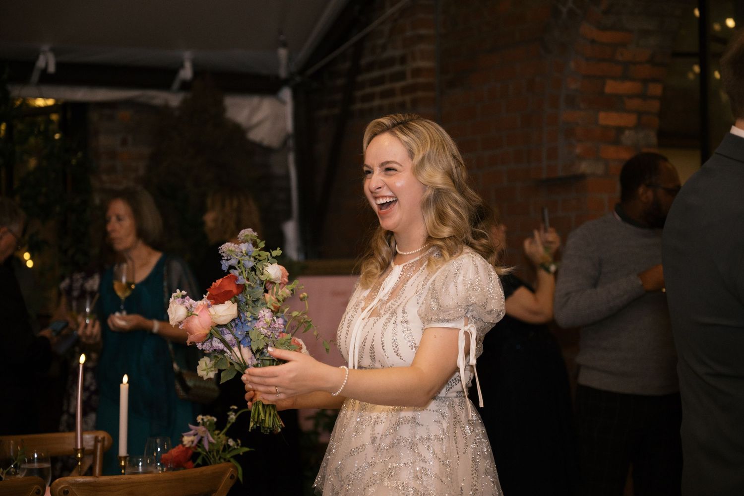 A joyful celebration moment at a wedding reception in an industrial-style venue with brick walls.