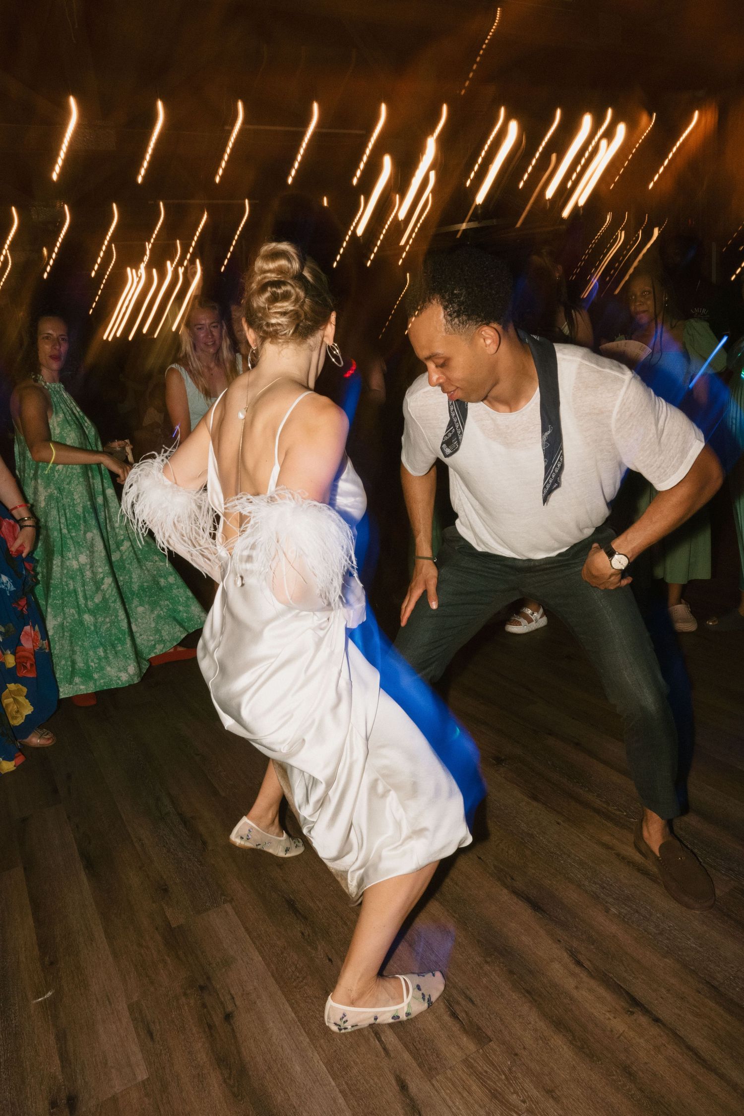 Dynamic dance moves on wooden floor with string lights creating ambient glow above.