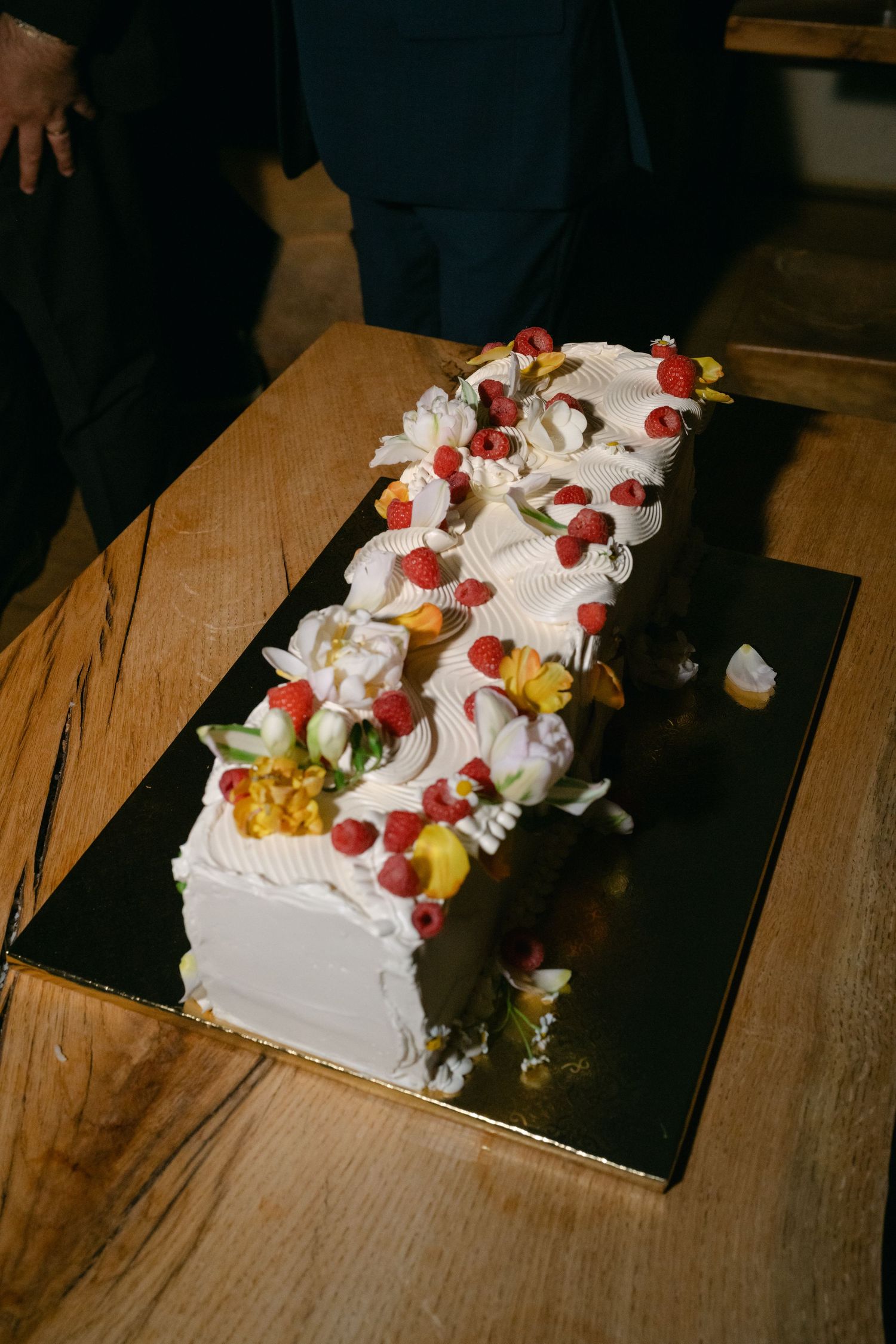Elegant white wedding cake decorated with fresh fruit and berries on a wooden table.