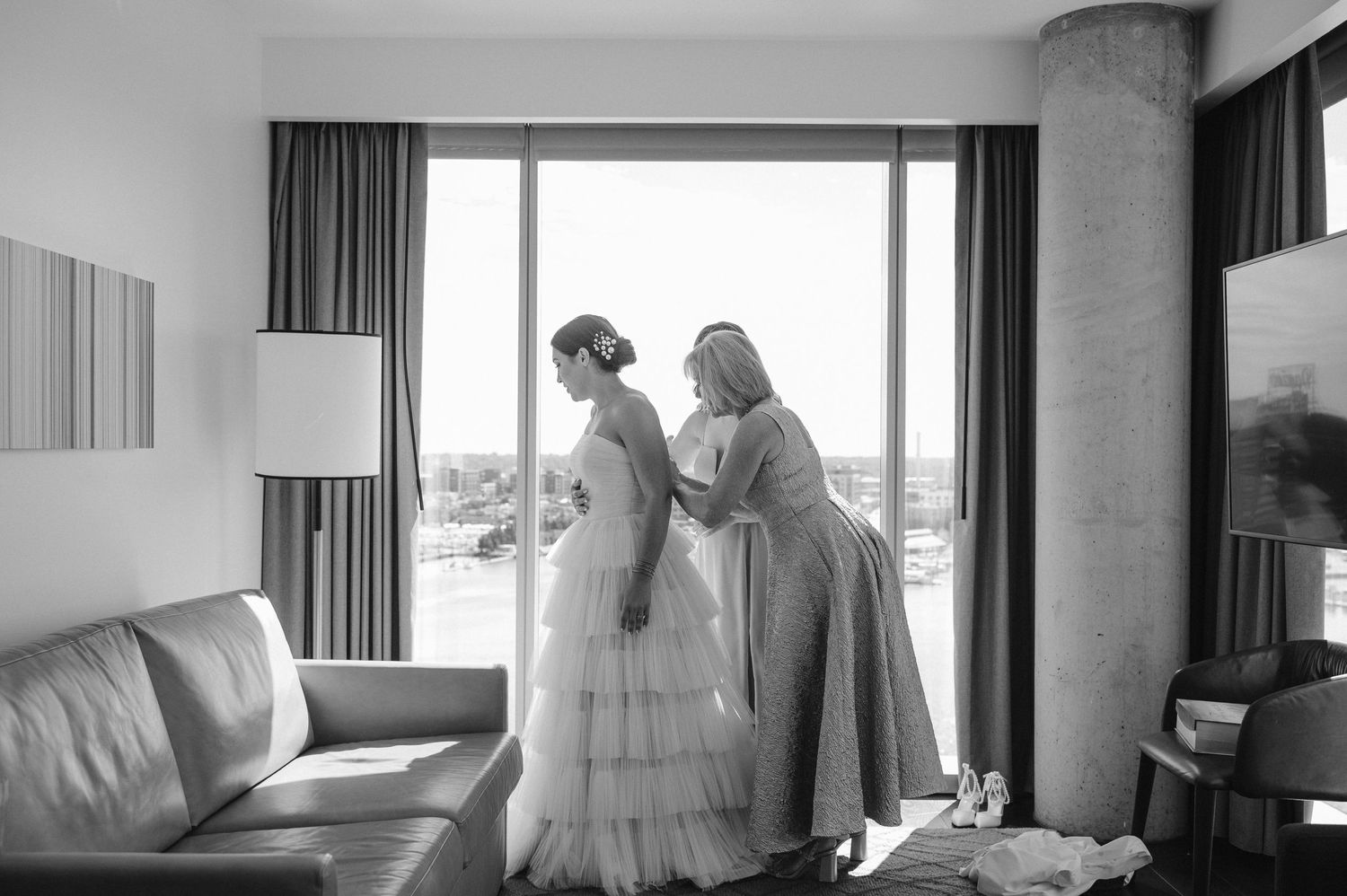 Black and white photo of wedding dress preparations in a modern hotel room.