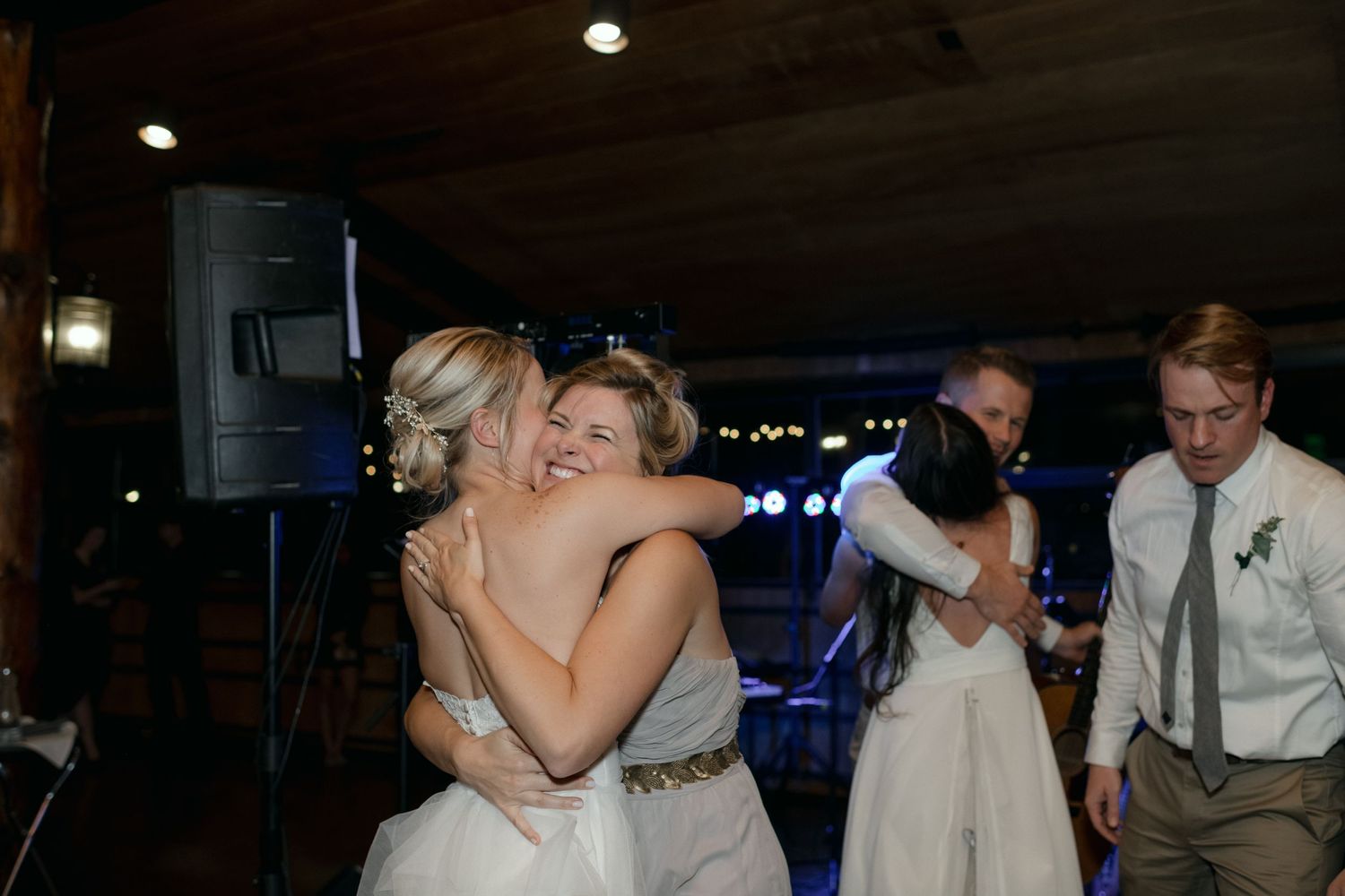 Wedding guests embracing on the dance floor during an evening reception with blue lighting.