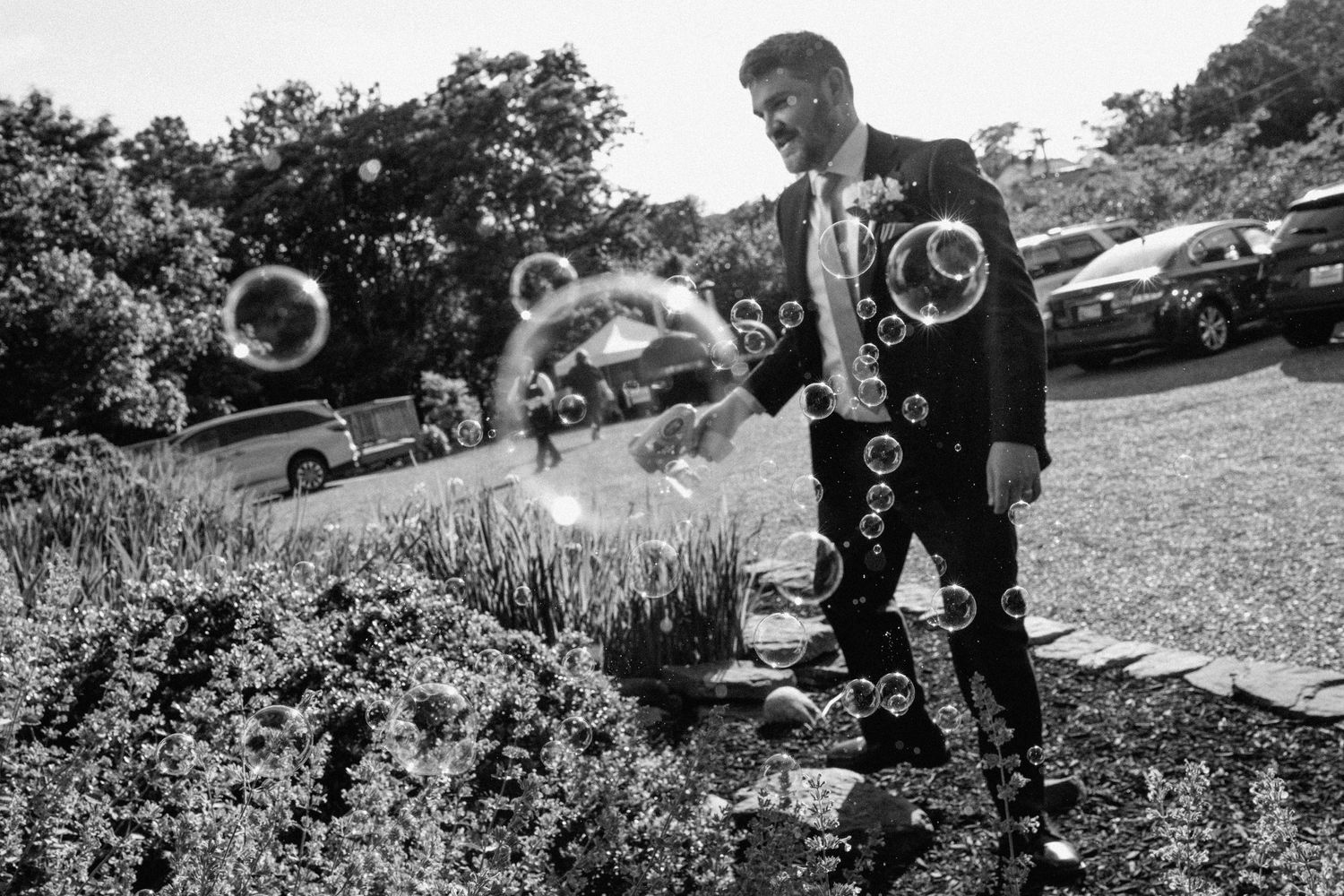 A person in formal wear plays with bubbles on a grassy outdoor setting.
