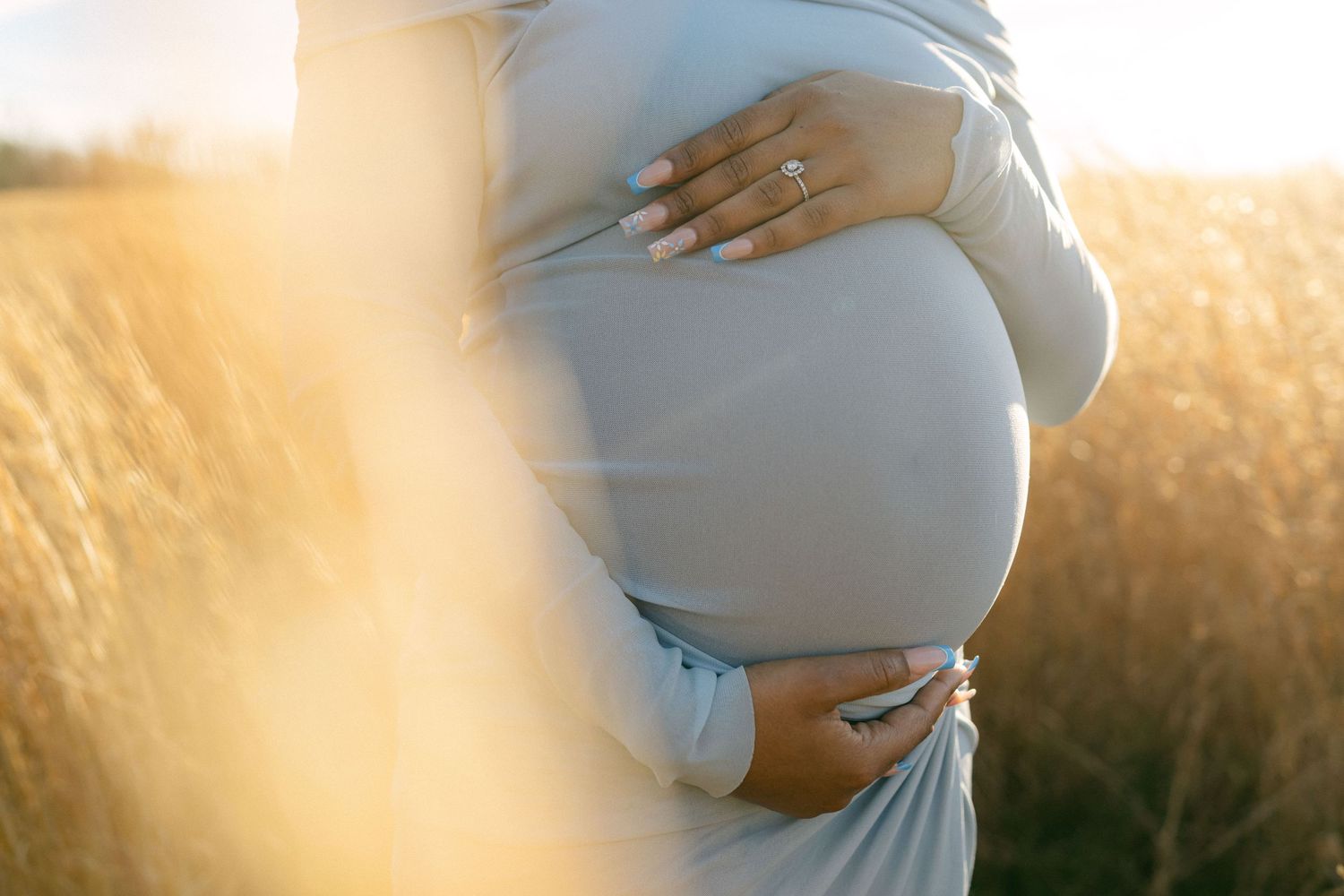 close up maternity photo of woman holding baby bump in field