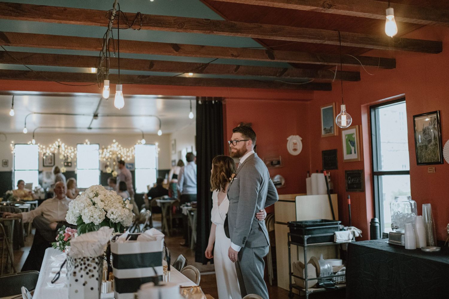 Wedding reception scene in a rustic venue with exposed wooden beams and warm lighting.
