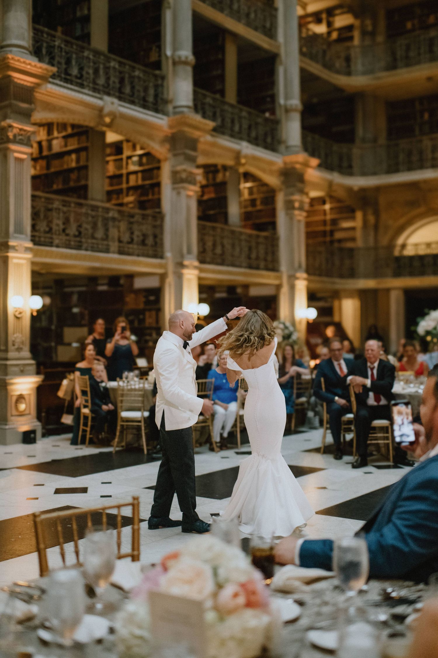 Wedding dance in a grand historic library with checkerboard floor and gold columns.