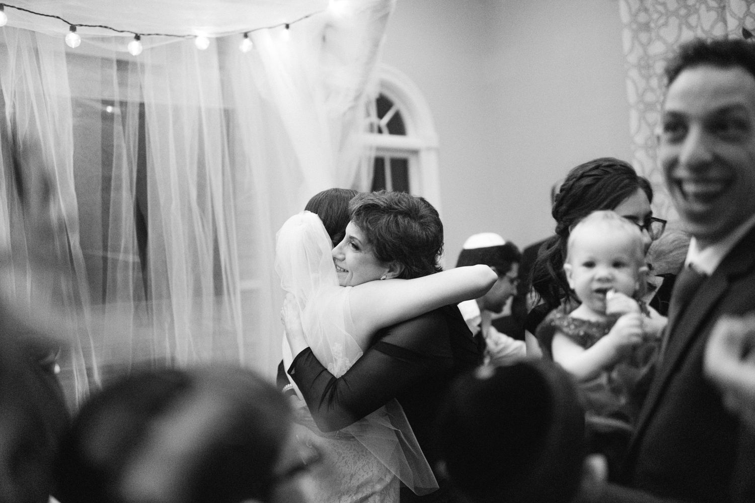 Black and white photo capturing joyful embrace during wedding celebration.