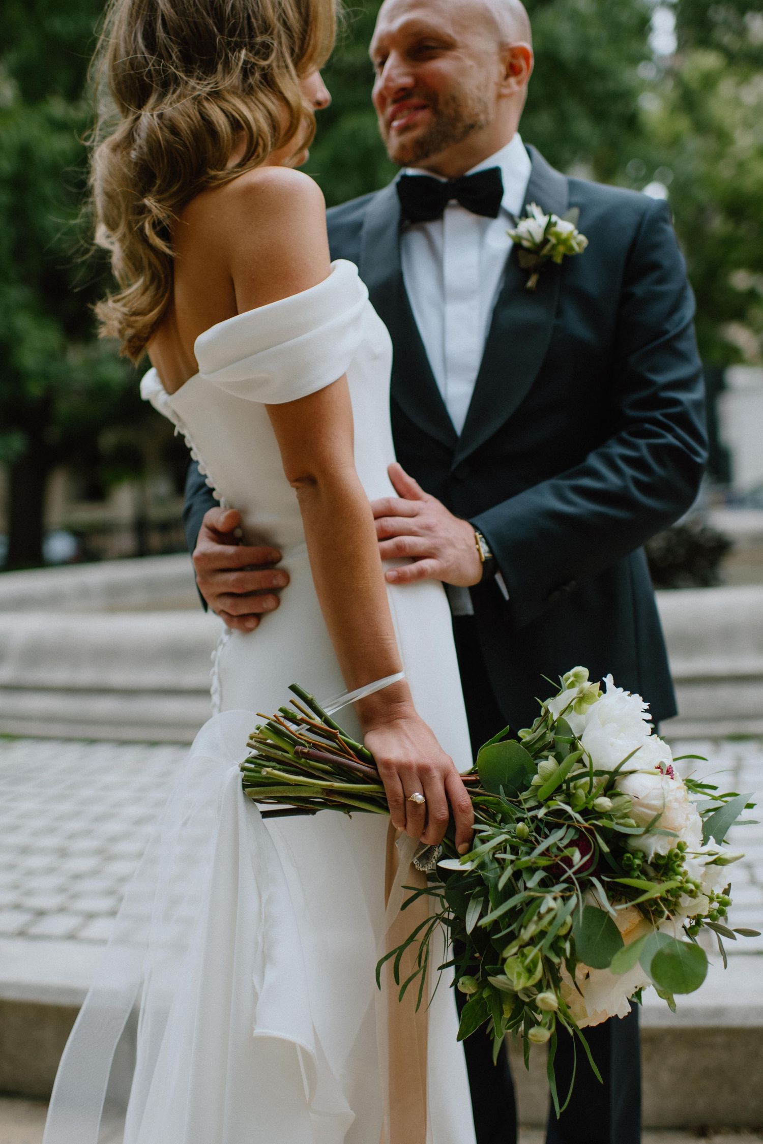 Close-up of newlywed couple embracing with bride holding white floral bouquet.