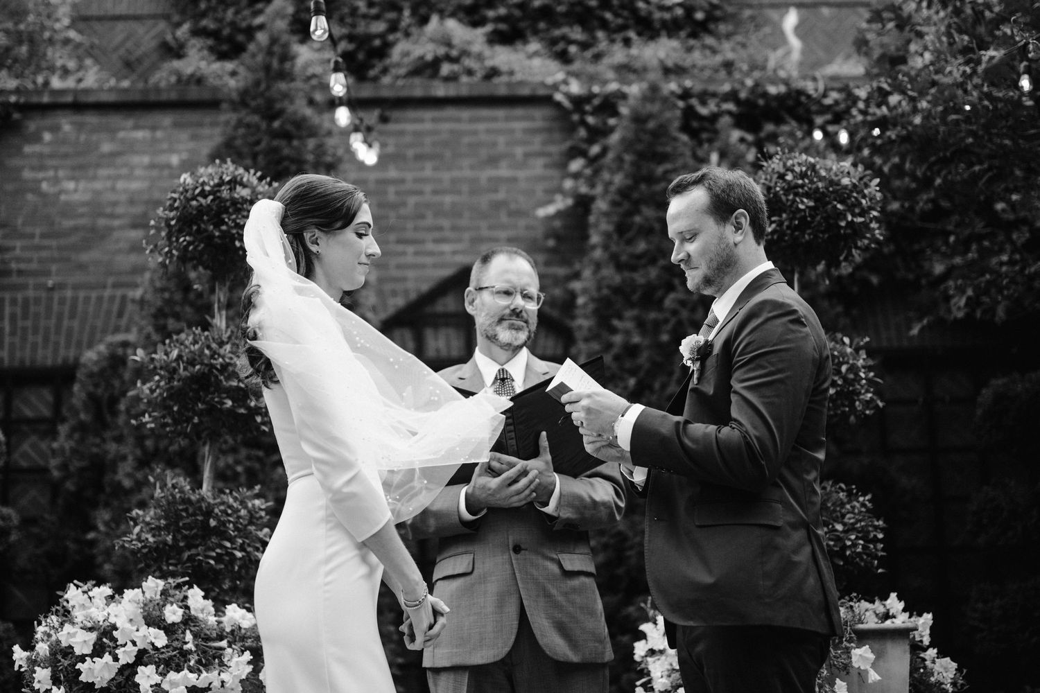 Black and white photo of a couple exchanging rings during their garden wedding ceremony.